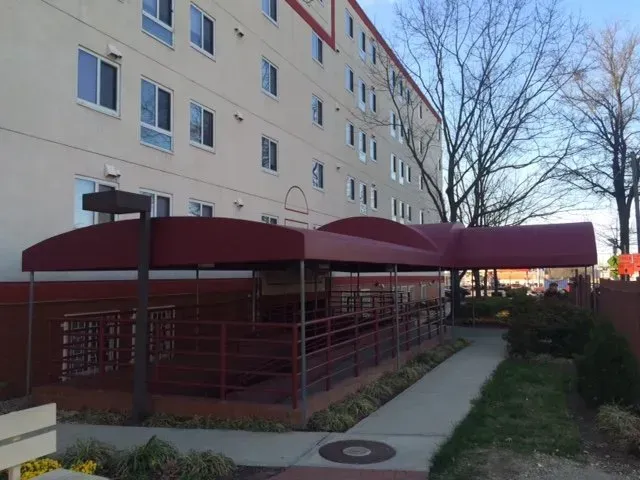 Covered red bike shelter beside apartment building along a sidewalk at dusk