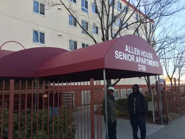 Entrance to Allen House Senior Apartments with red awning and two people standing under it