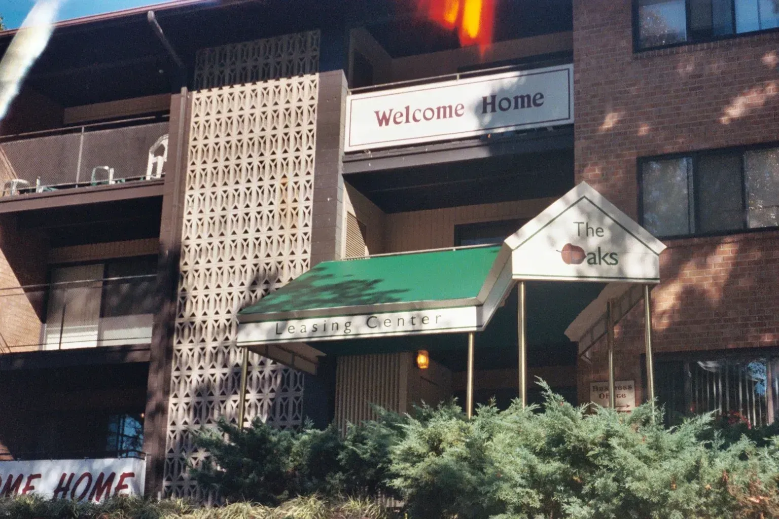 Brick building entrance with green awnings and a “Welcome Home” sign above the door