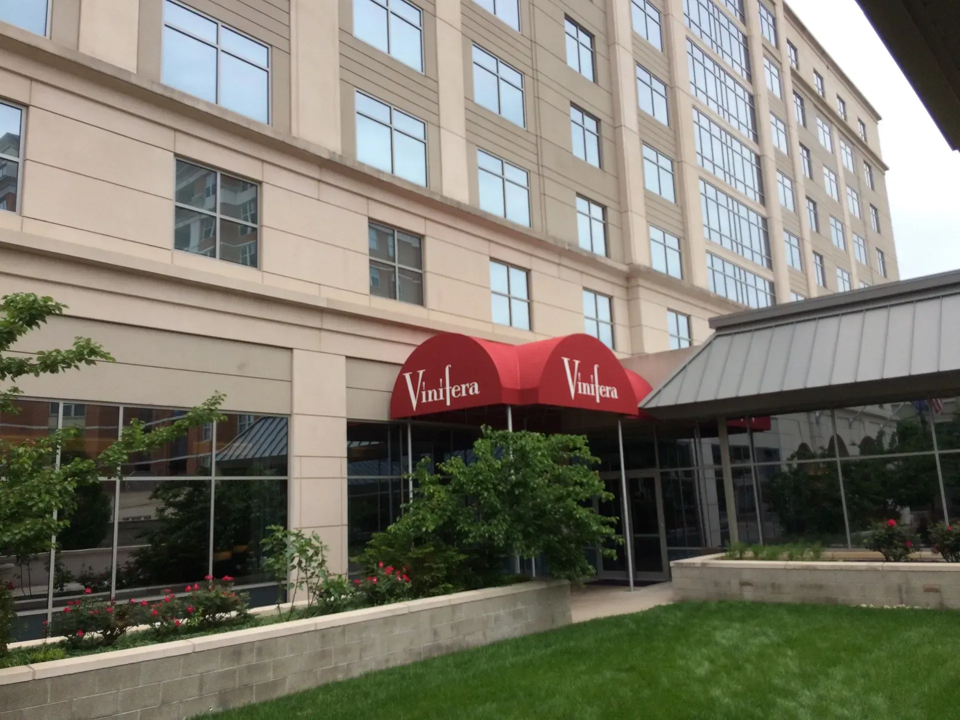 Hotel entrance with red awning and glass canopy beside a tan multi-story building