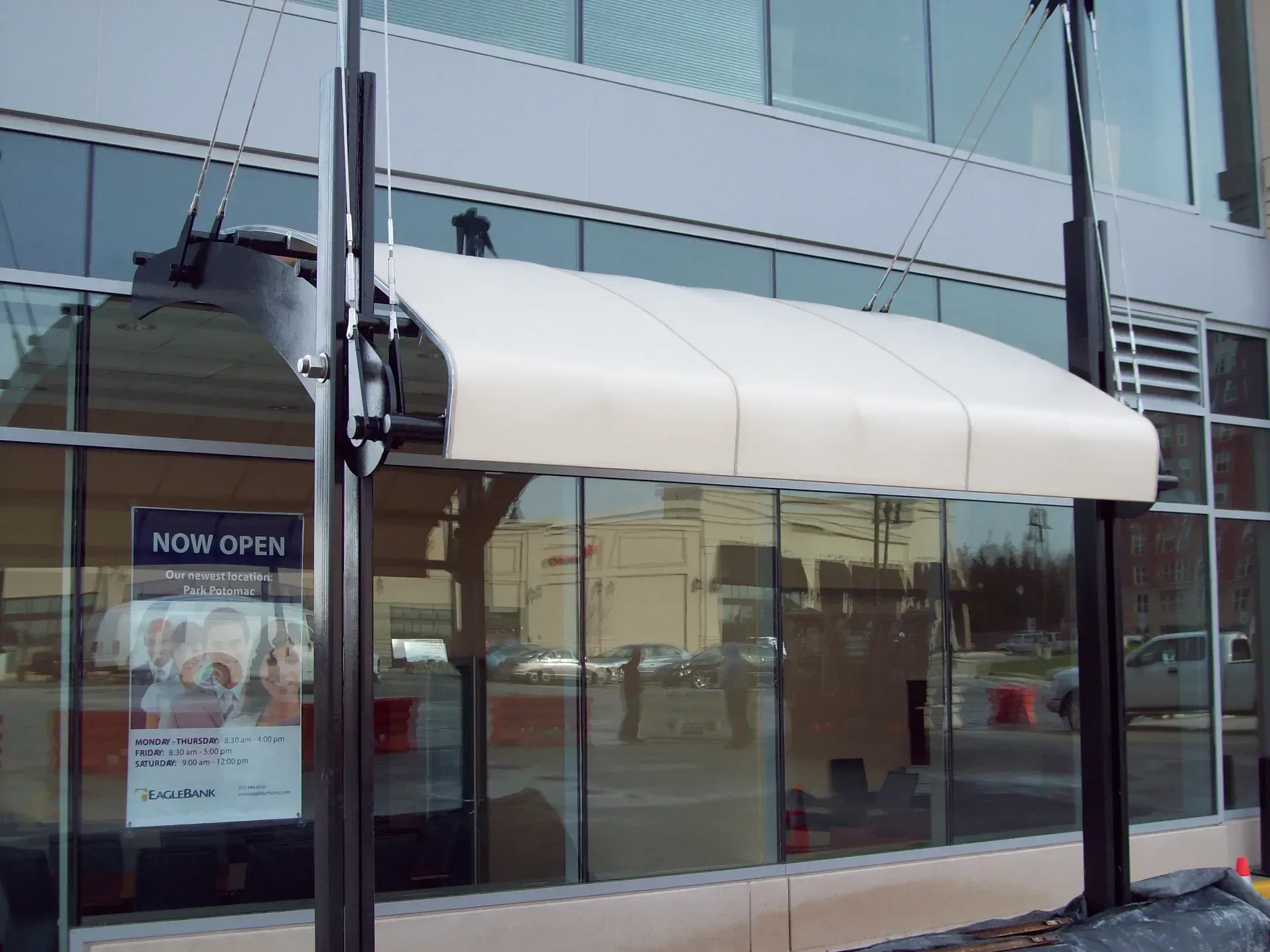 Storefront with a white awning and glass windows, featuring a “Now Open” sign.