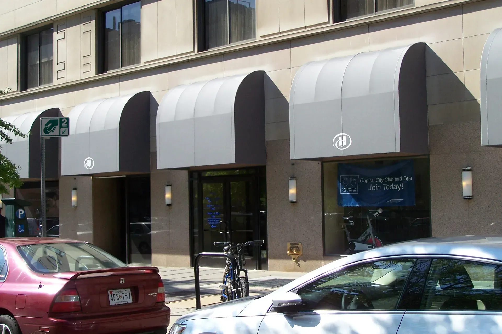 Storefront with gray awnings on a city street, with parked cars in front.