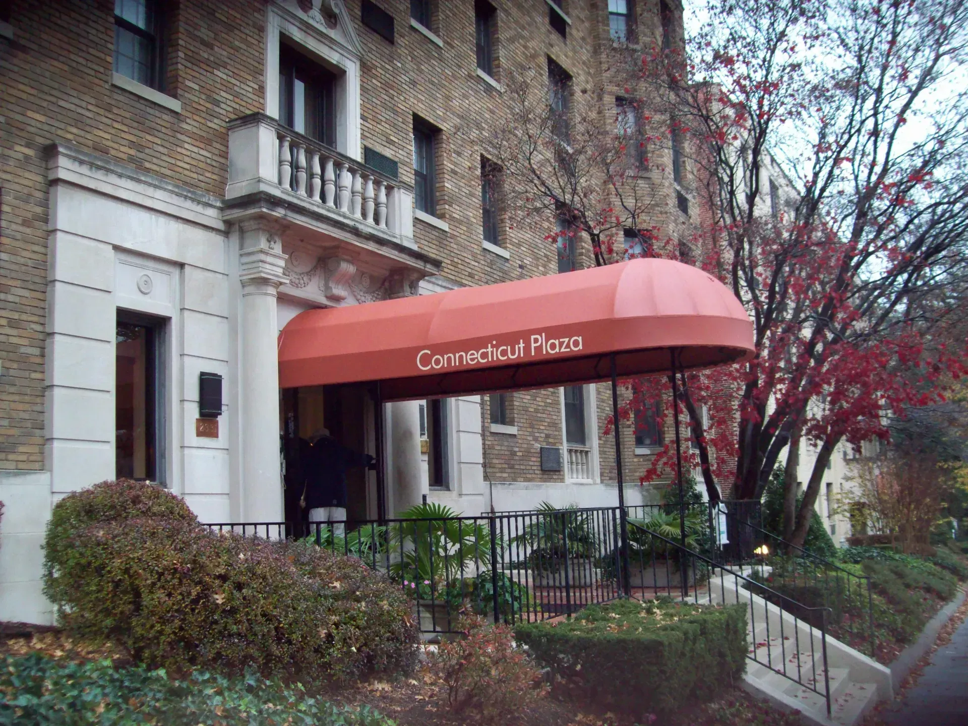 Brick apartment entrance with red awning reading “Country of Pizza,” steps, railing, and bare trees.
