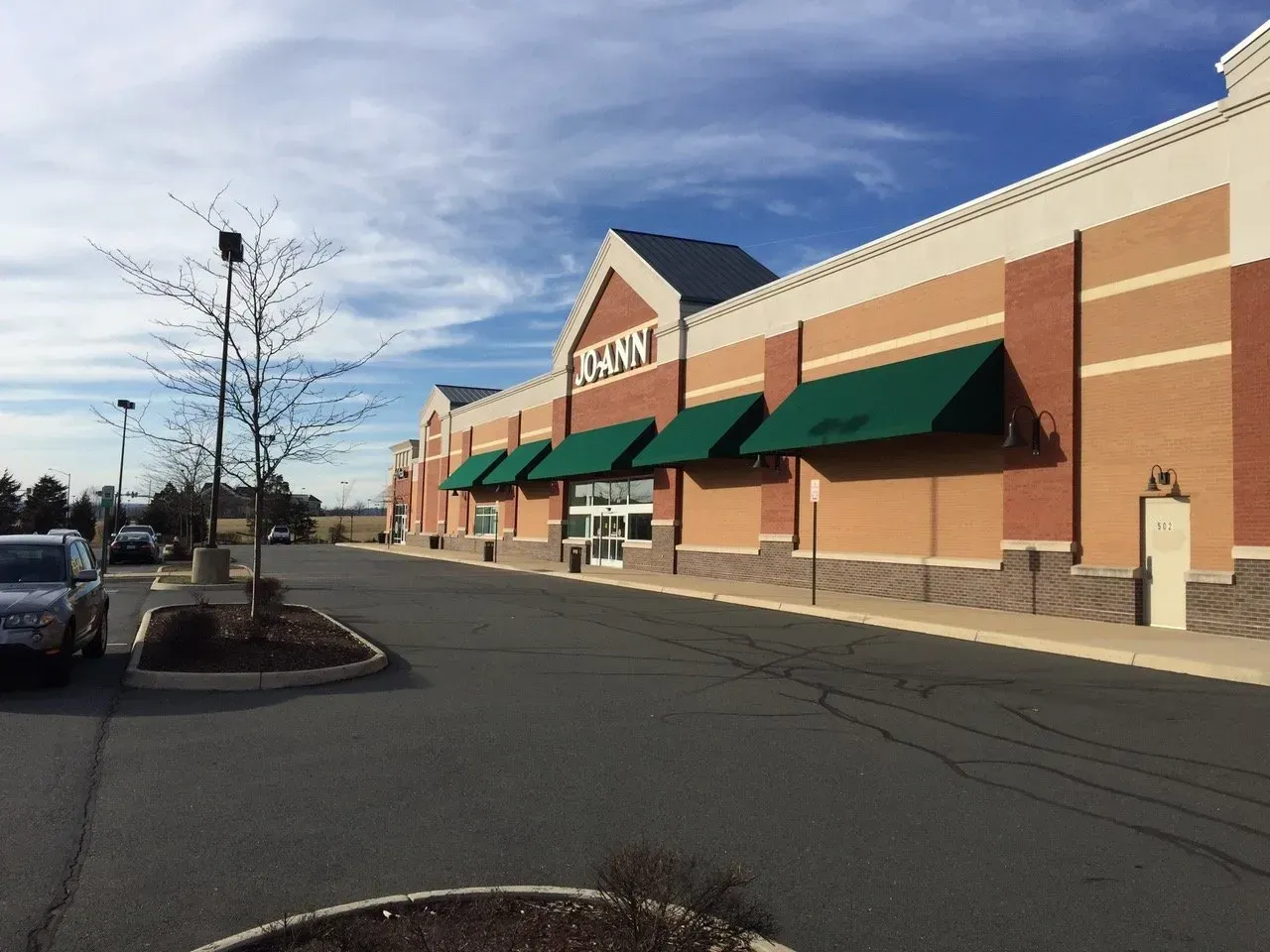 Strip mall storefront with green awnings and parked cars under a blue sky