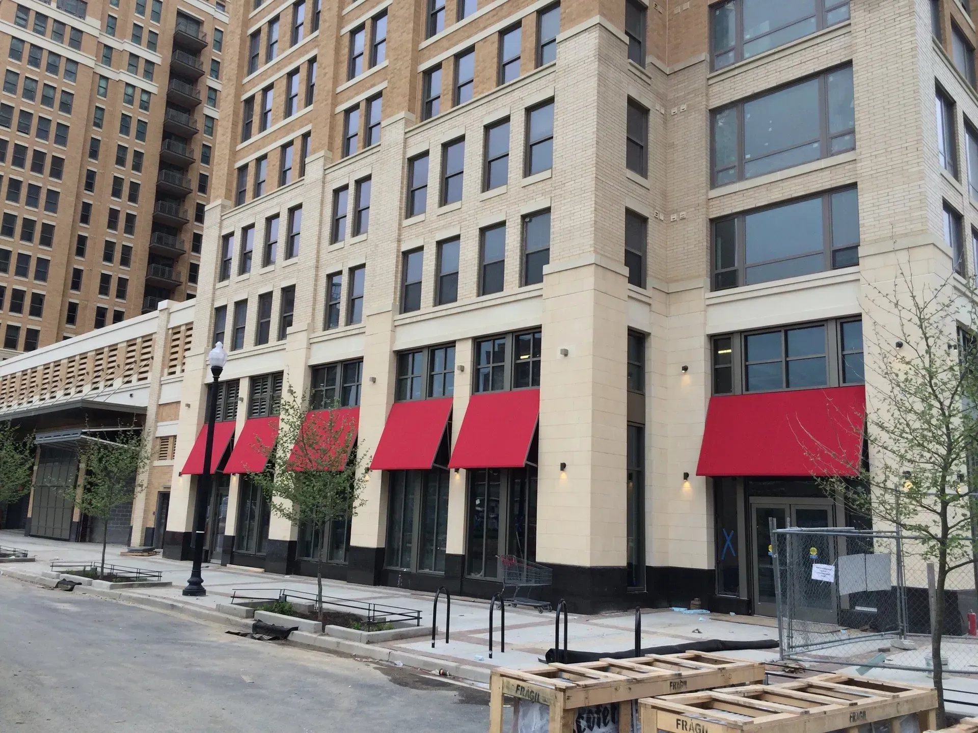Street-level view of a beige apartment building with red awnings and glass storefronts under construction