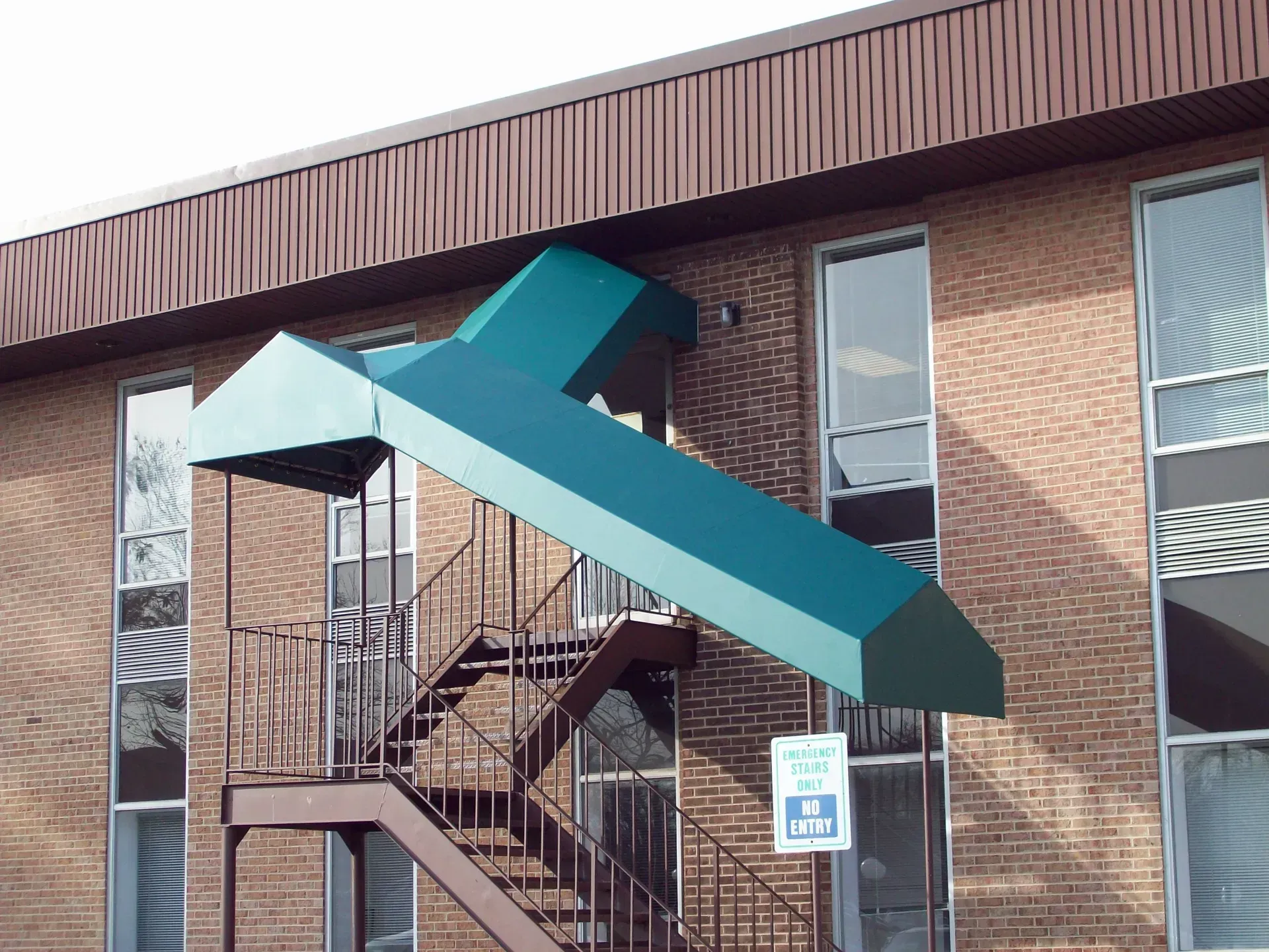 Brick building with exterior metal stairs and teal awnings over the stair landing.