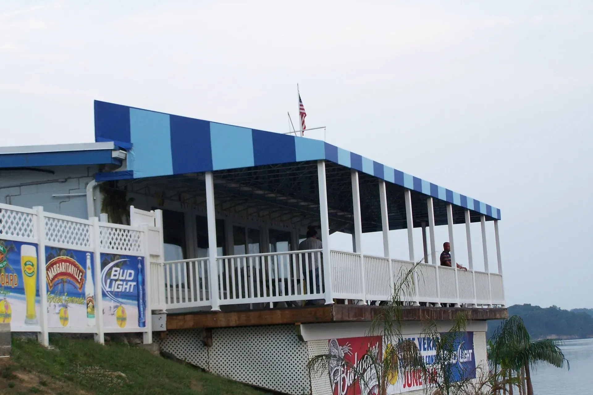 Blue-and-white waterfront building with a covered balcony and signs on the lower level