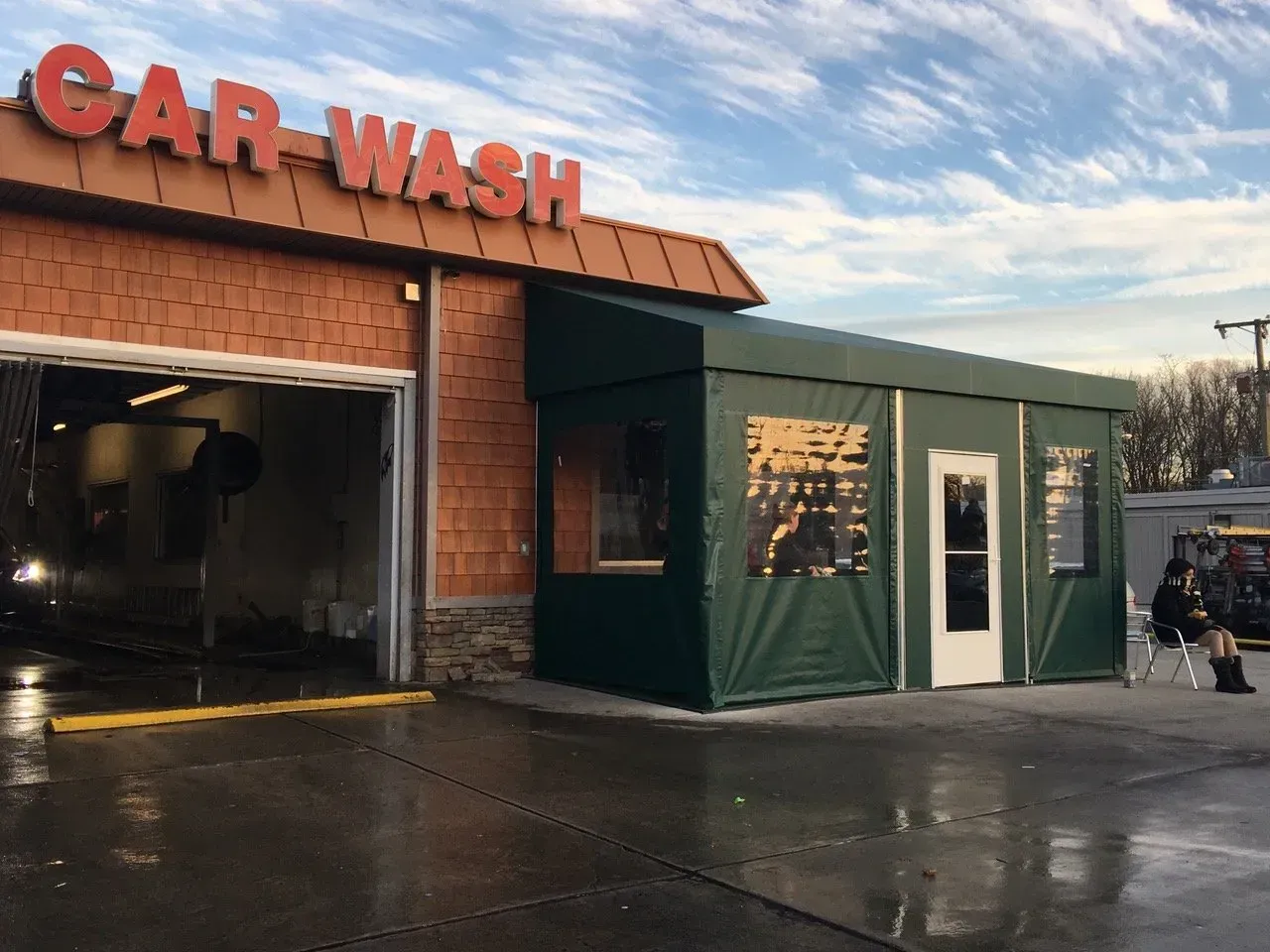 Car wash building with a red sign, open bay, green side structure, and wet pavement at dusk