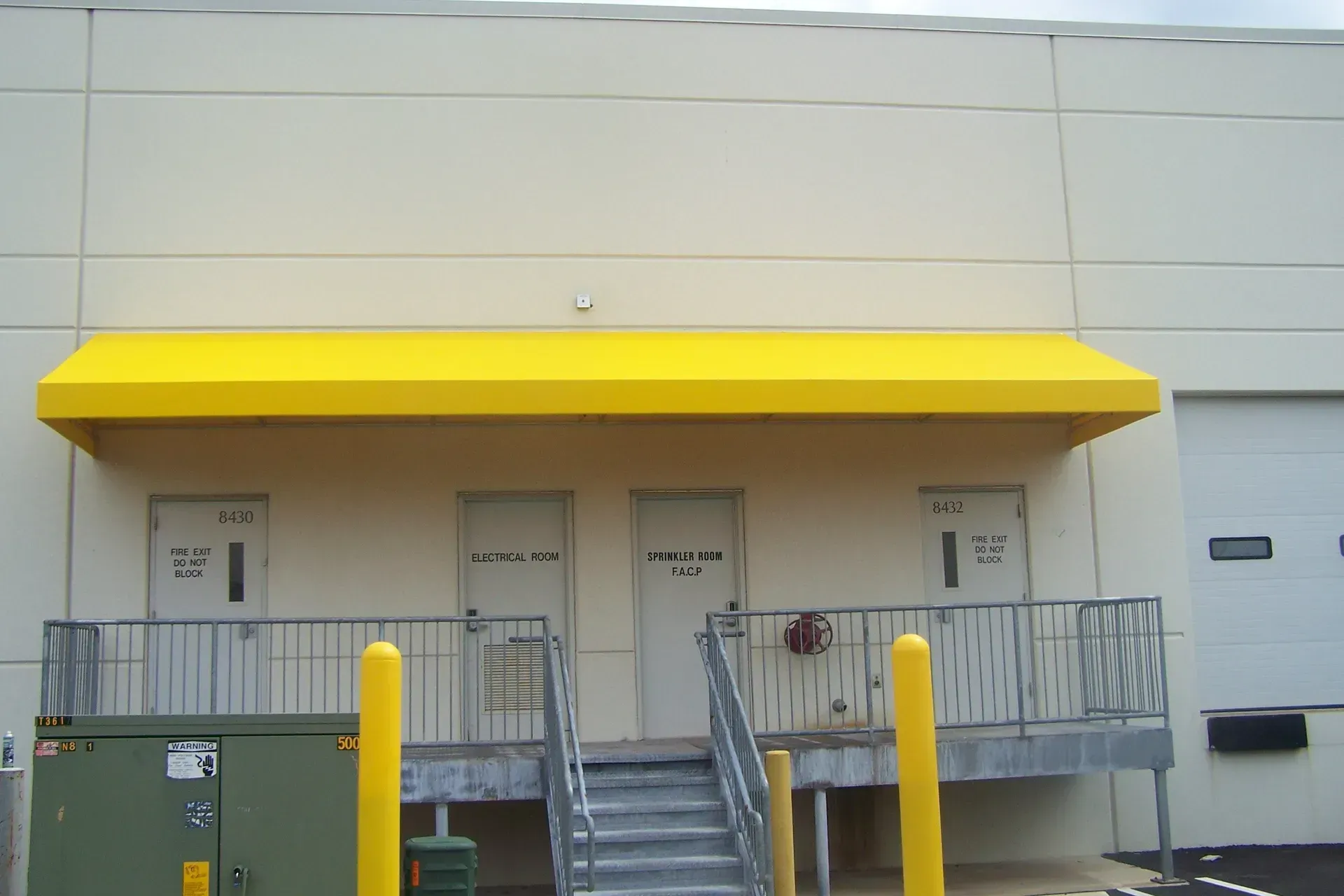 Industrial loading dock with yellow awning, metal platform, and stairs at a warehouse loading area