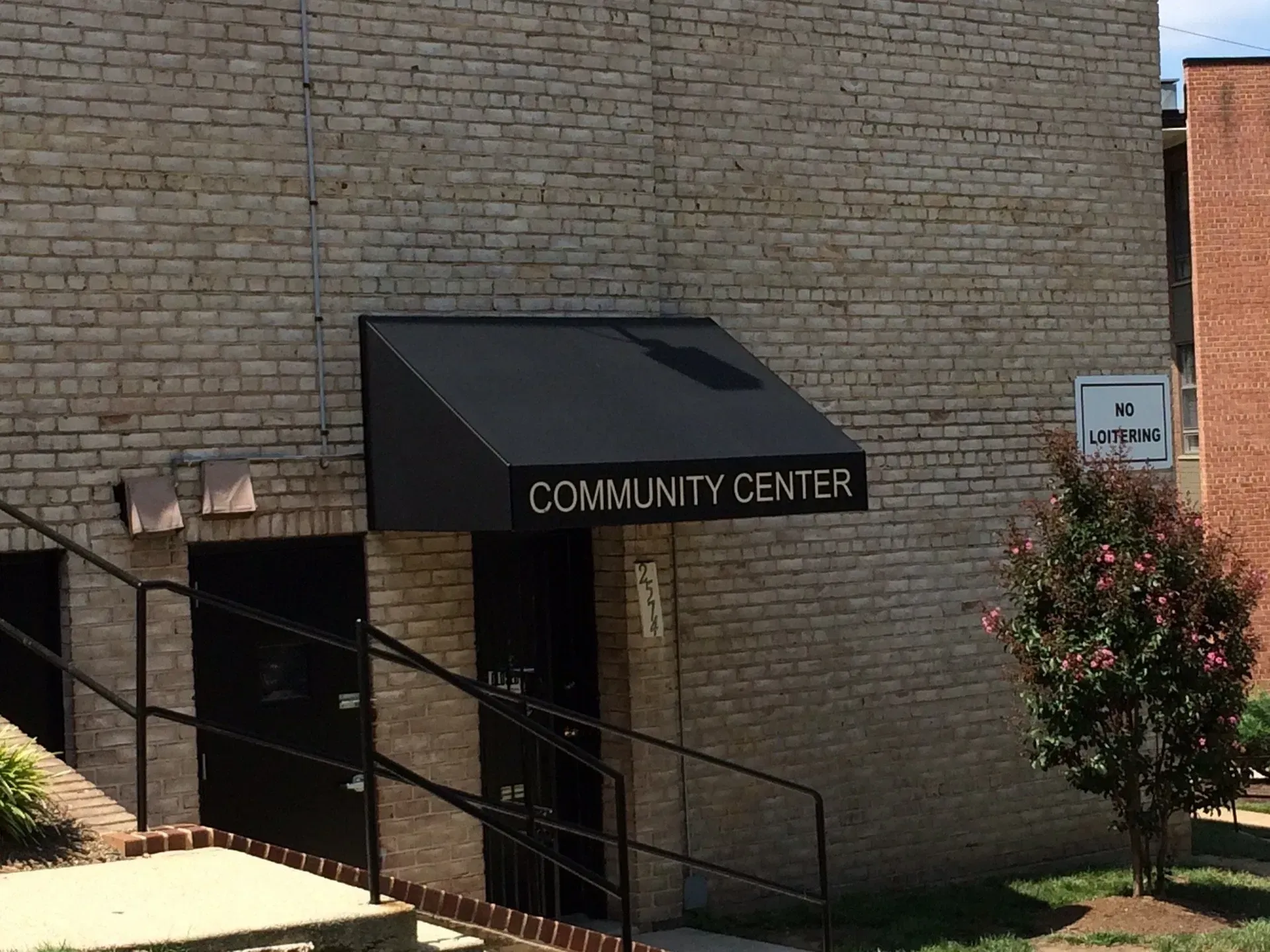 Brick building entrance with black awning labeled “Community Center” and stairs with railing