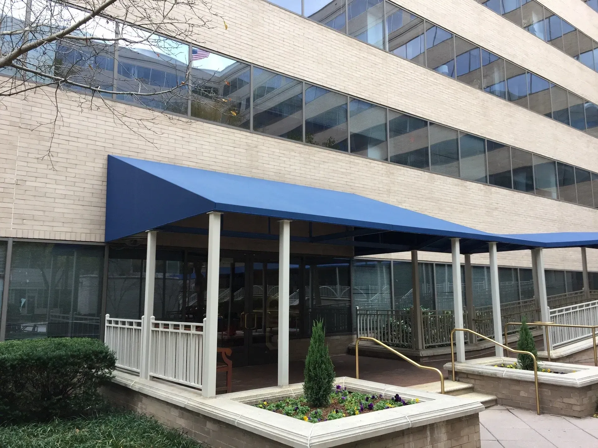 Building entrance with blue awning, glass windows, and a small landscaped planter in front