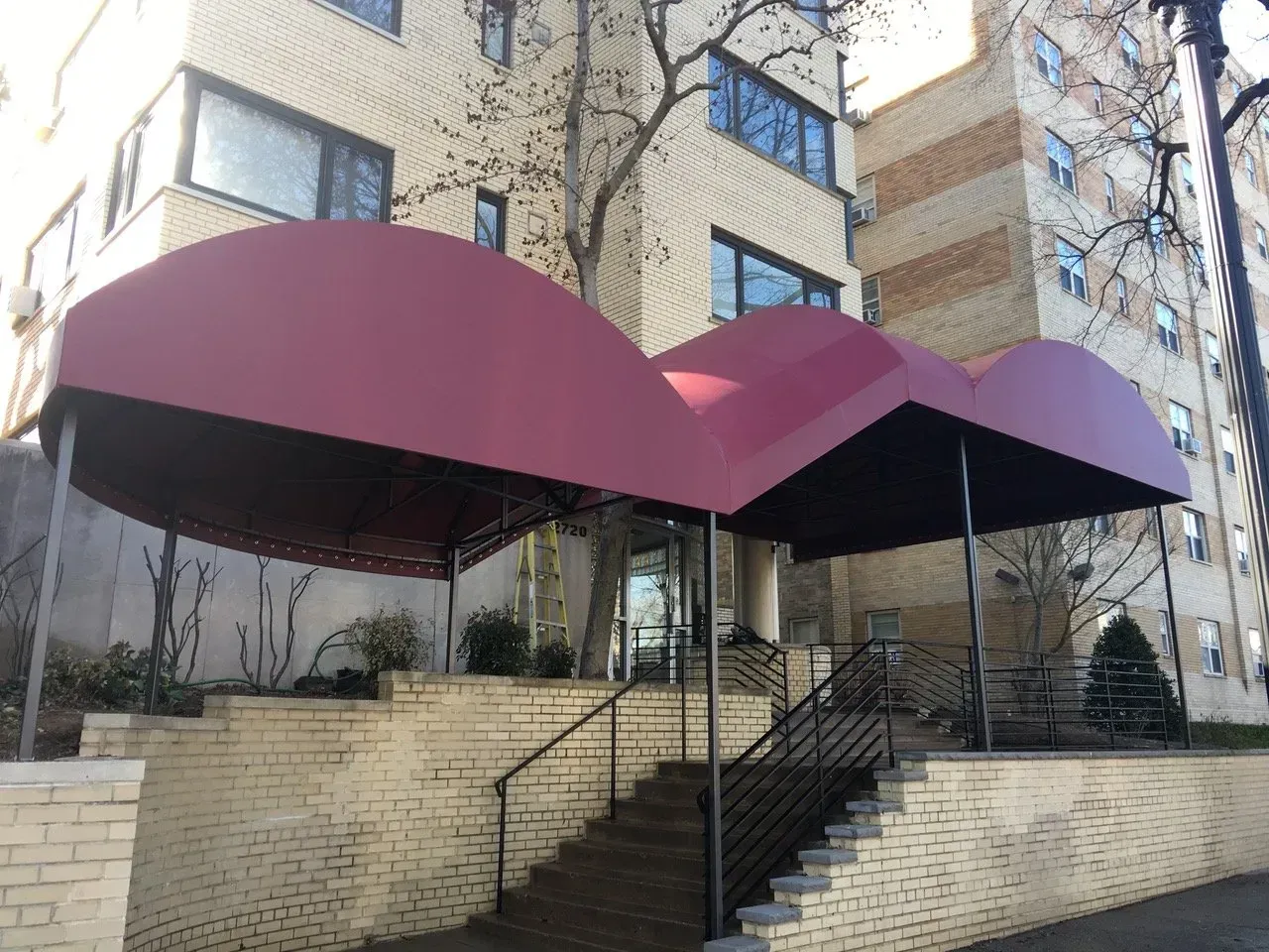 Apartment entrance with burgundy awnings, stairs, and brick retaining walls