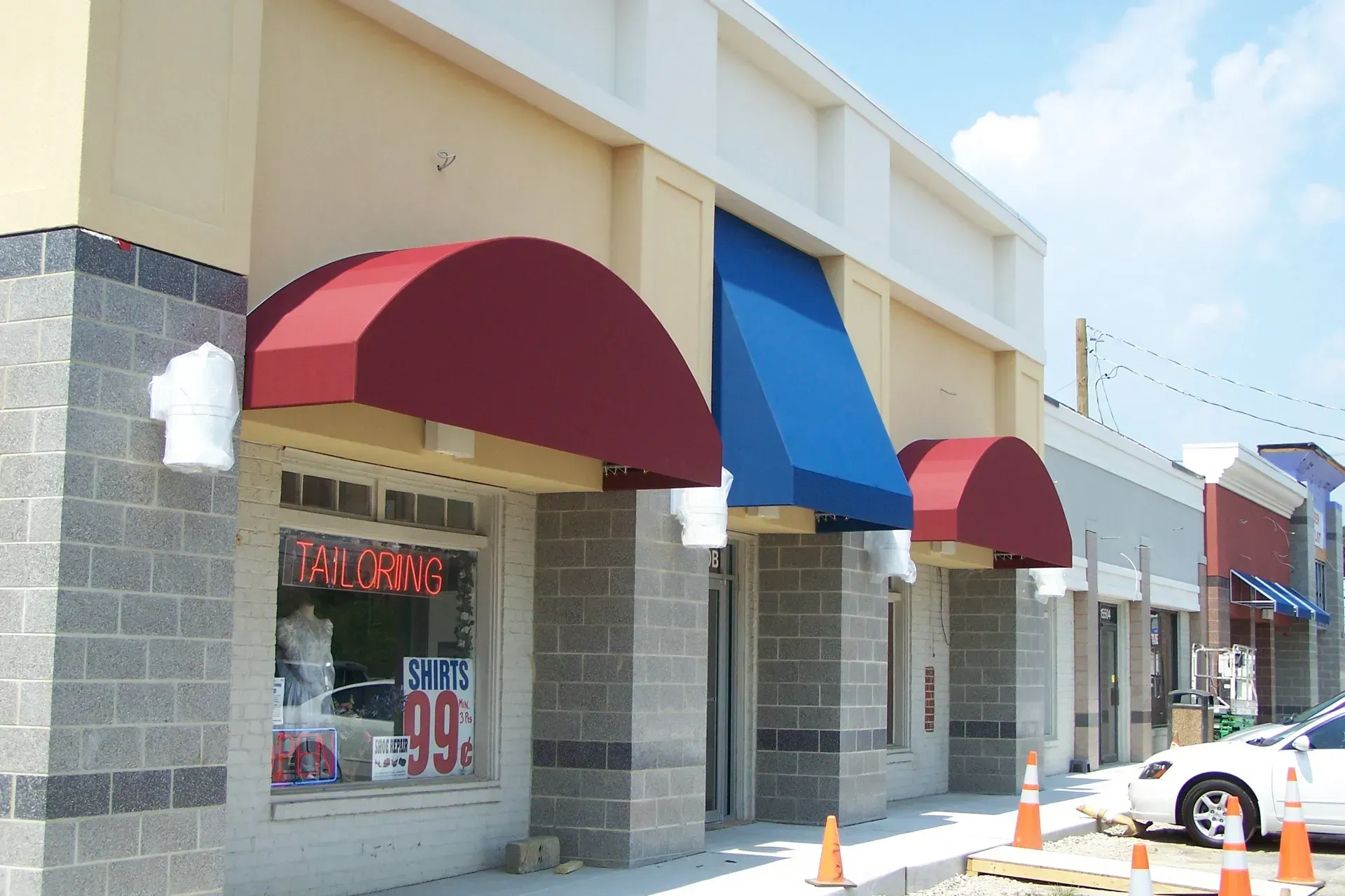 Storefronts with red and blue awnings along a sunny shopping center walkway