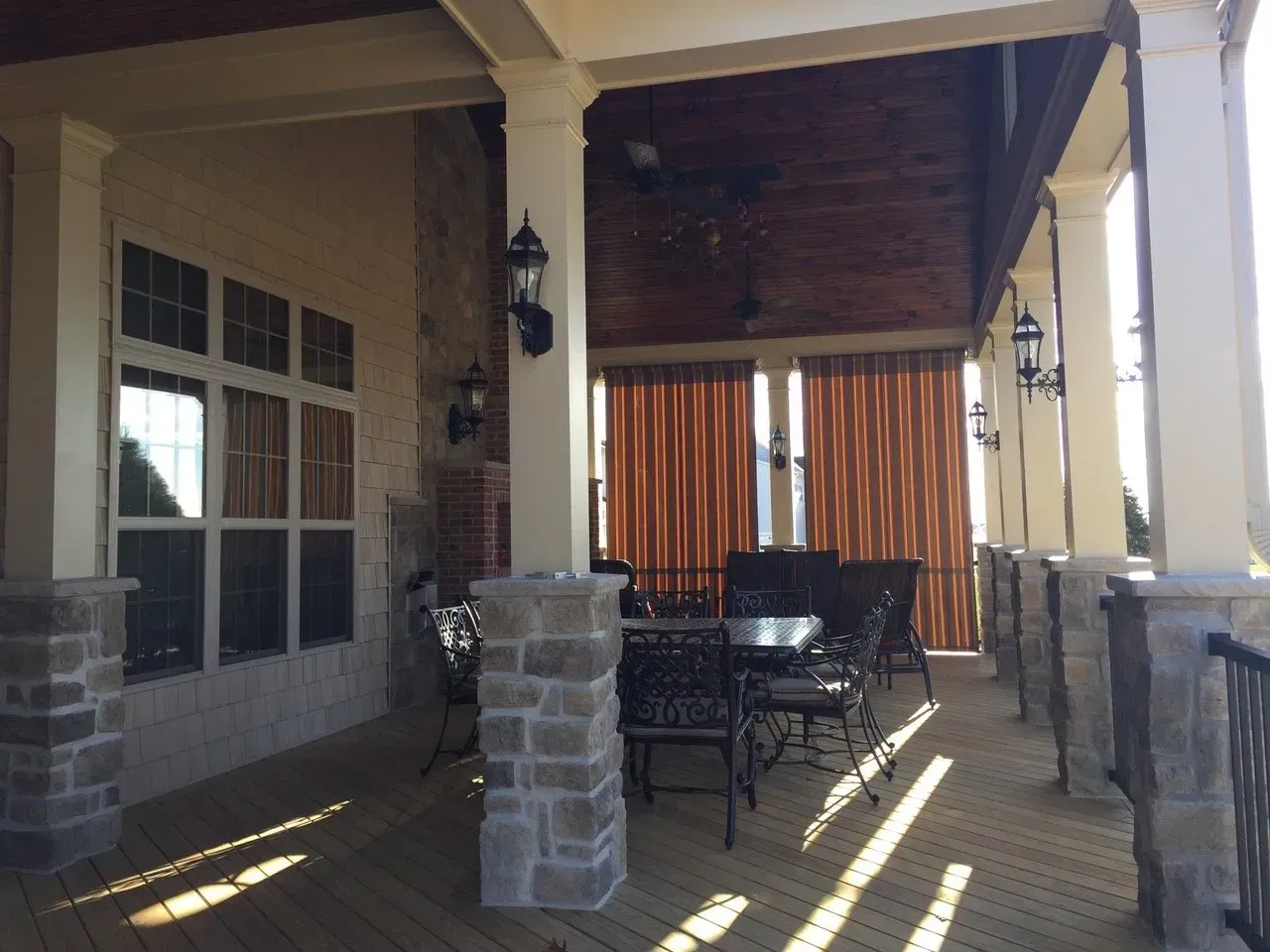 Covered patio with stone columns, table and chairs, and orange curtains in the background.