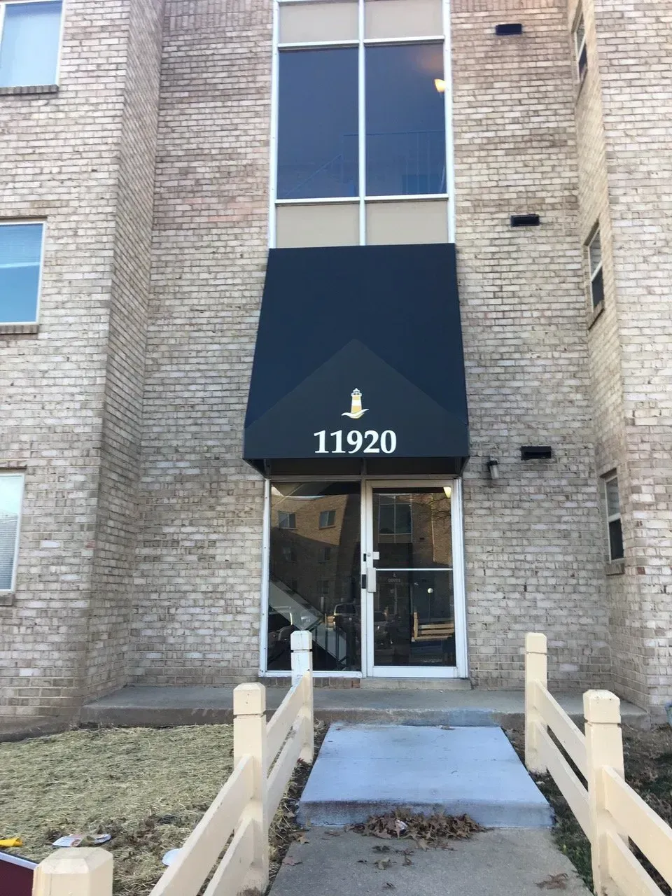 Apartment building entrance with black awning and address 11920 above a glass door.