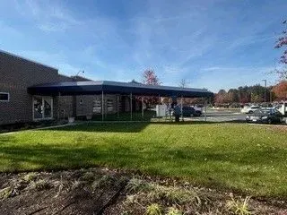 Brick building with covered entrance, grassy foreground, and parked cars under a blue sky.