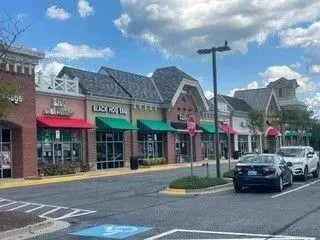 Small town shopping center with brick storefronts, parked cars, and a cloudy sky.