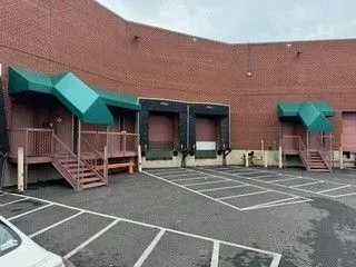 Loading dock with green awnings, brick wall, and empty parking spaces behind a building
