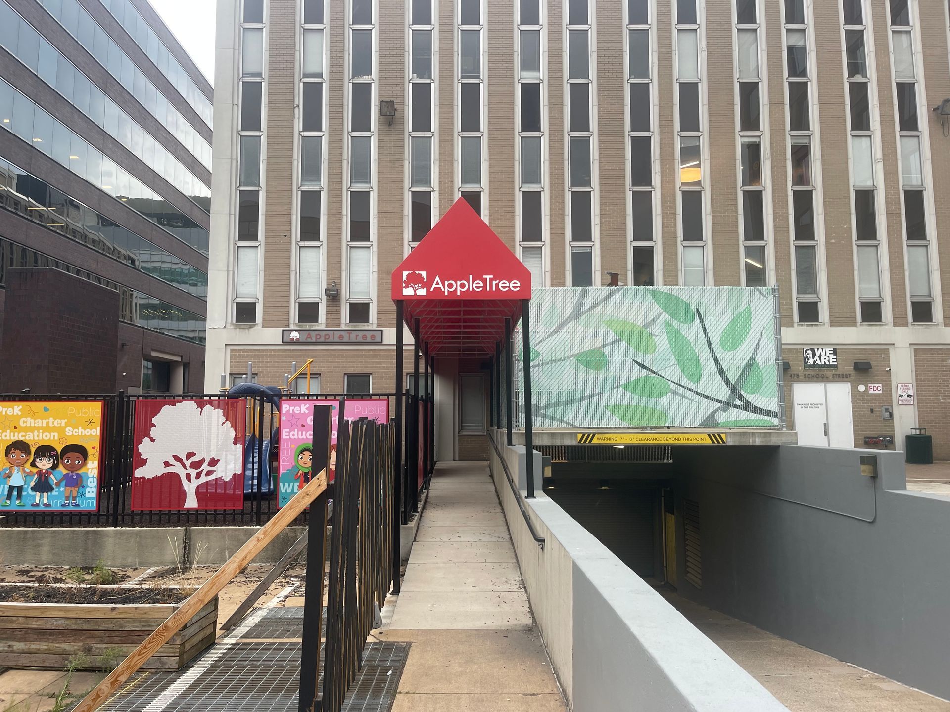 Ramp leading to a building entrance with a red awning, flanked by colorful outdoor signs in an urban plaza.