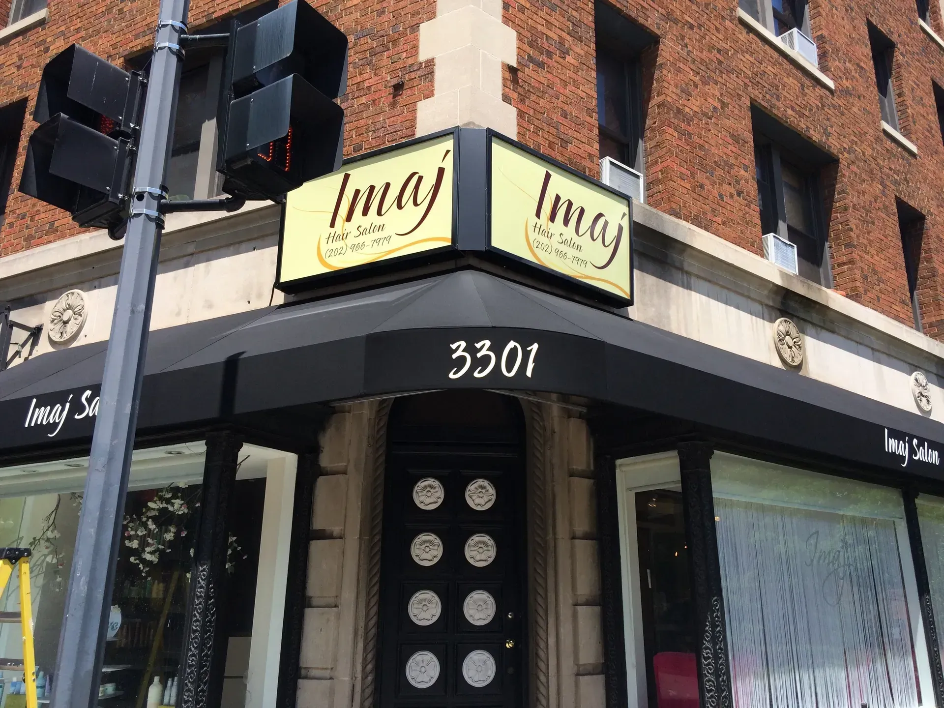 Storefront corner with yellow “Imaj” signs, black awning, and address 3301 on a brick building