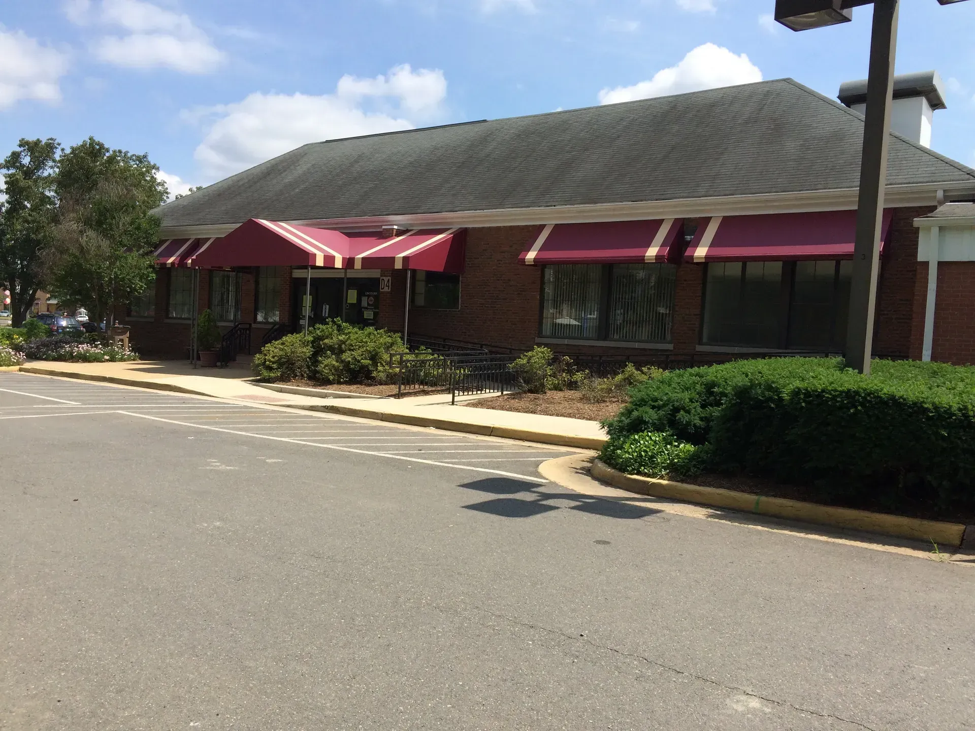 Single-story brick building with red awnings beside an empty parking lot under a blue sky