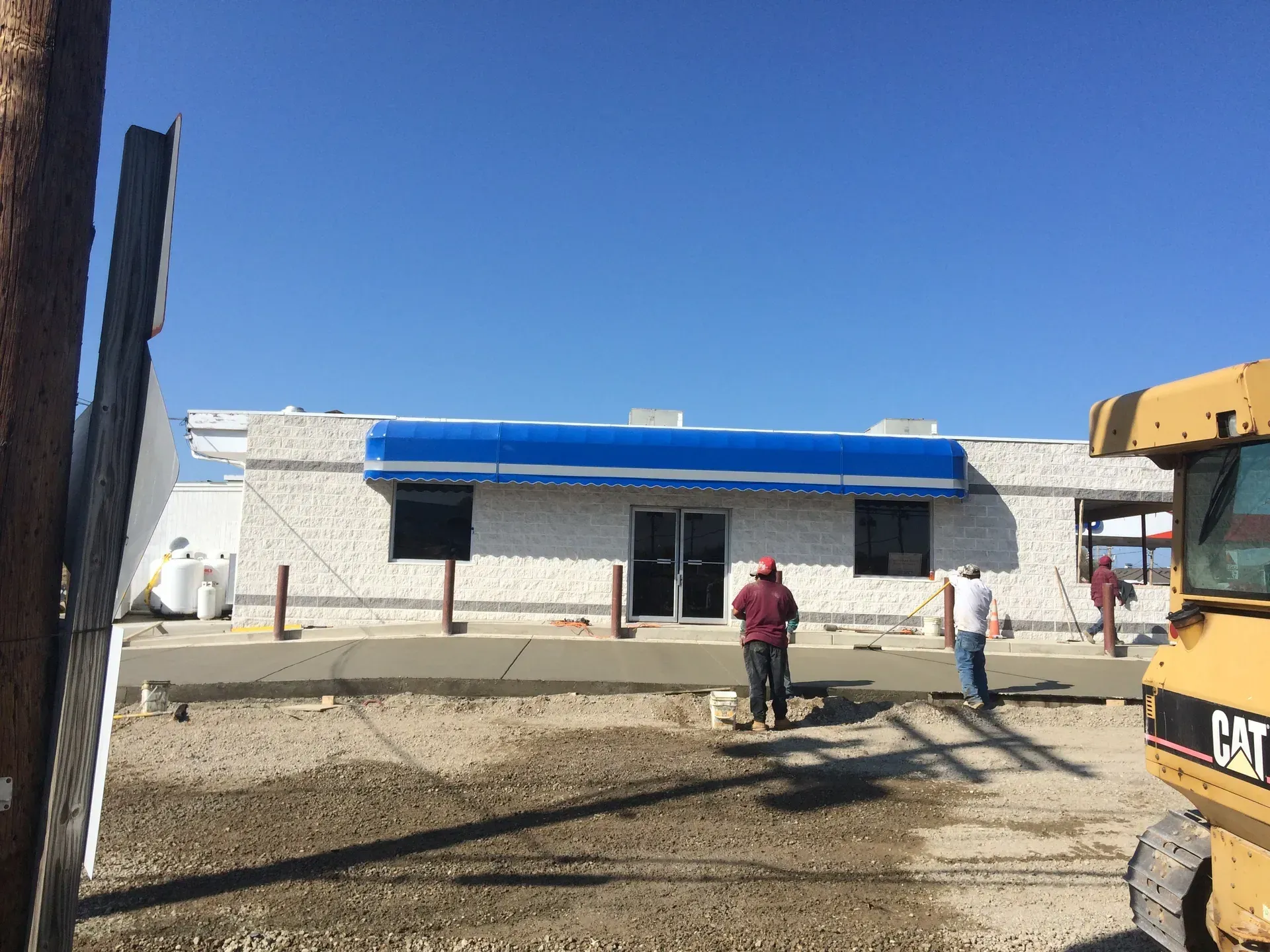 Construction site with a small white building, blue roof, and two workers standing in front.