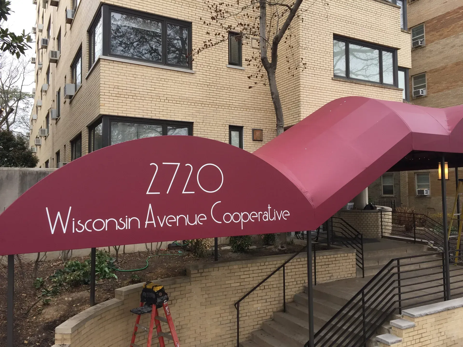 Entrance to 2720 Wisconsin Avenue Cooperative with maroon awning and brick apartment building