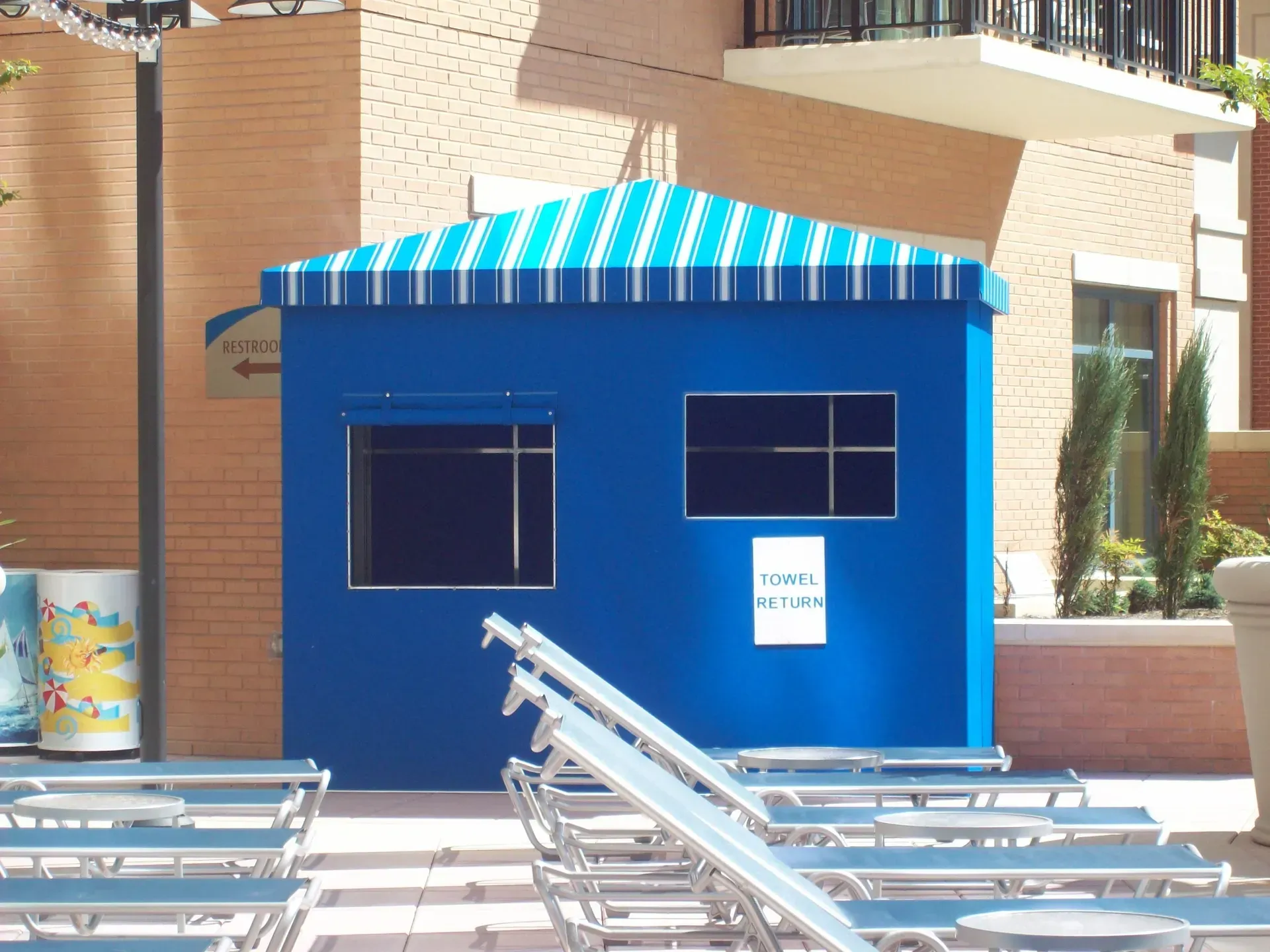 Blue kiosk with striped awning beside pool lounge chairs outdoors