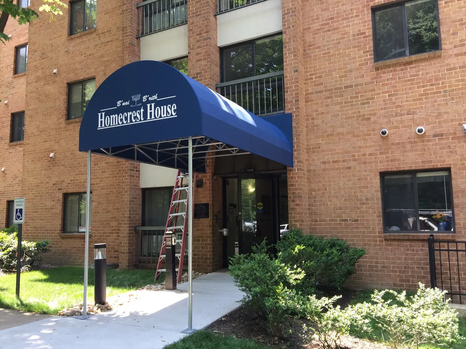 Blue awning over apartment entrance with ladder on sidewalk beside brick building