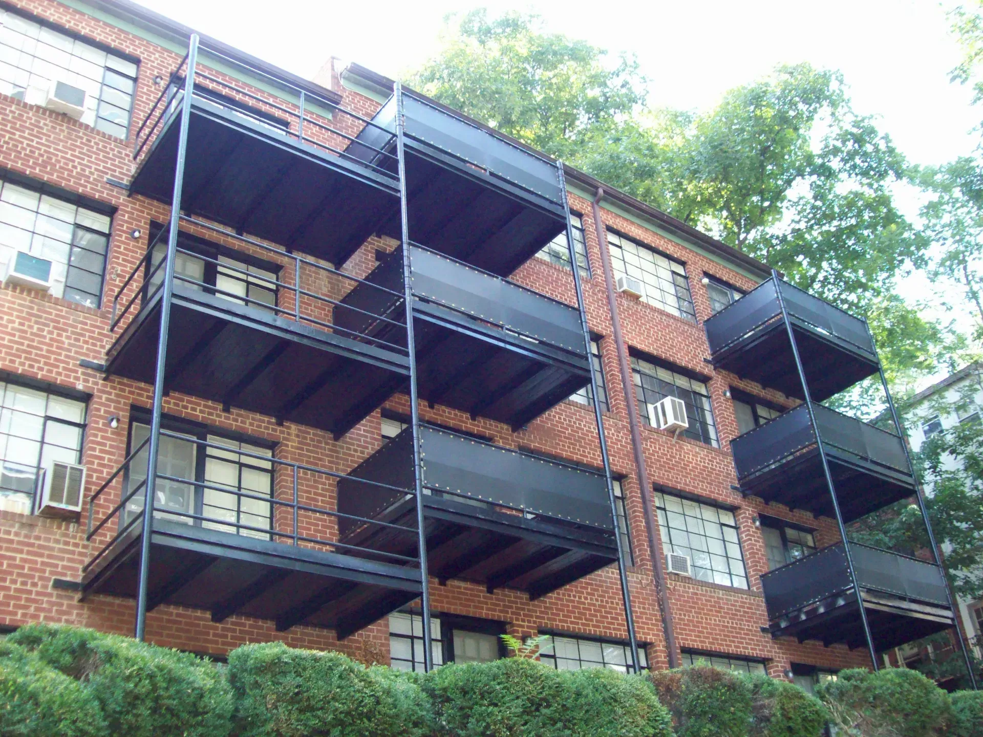Brick apartment building with black metal fire escapes and balconies, viewed from below amid trees