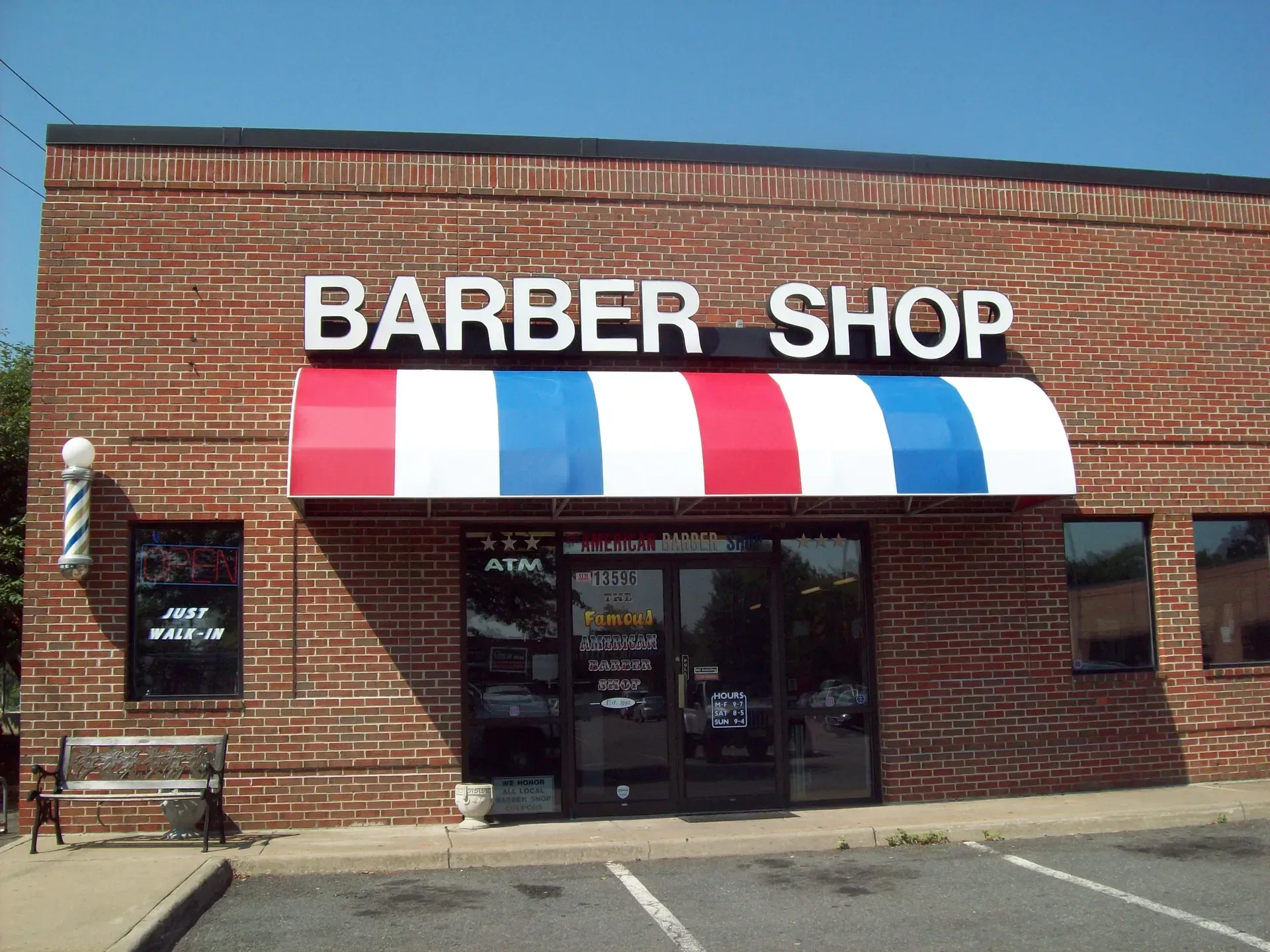 Brick storefront barber shop with red, white, and blue striped awning.