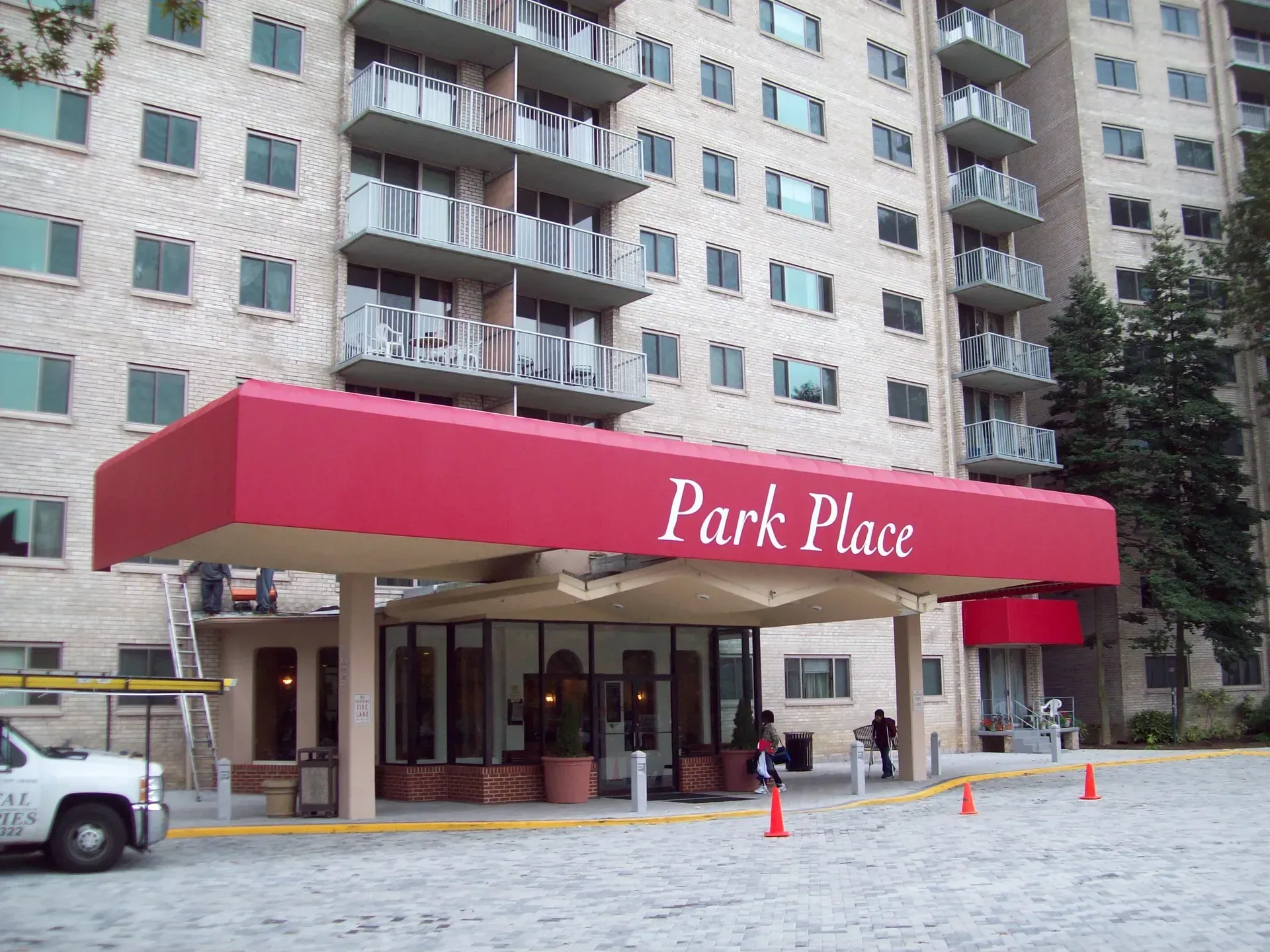 Entrance canopy reading “Park Place” at a high-rise building, with parked cars and orange cones outside.