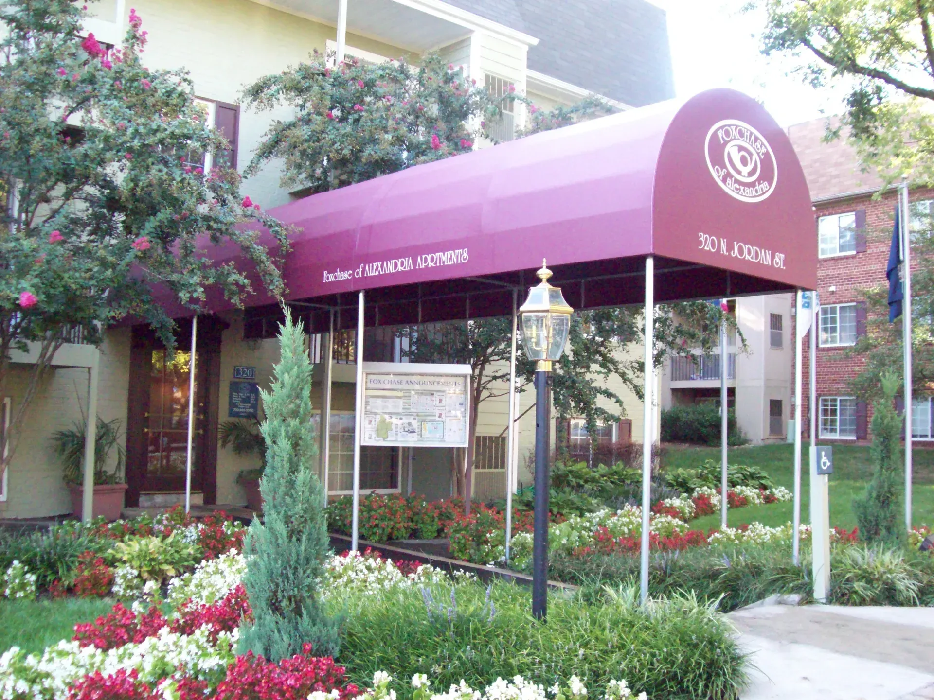 Building entrance with a purple awning, flower beds, and a landscaped garden courtyard