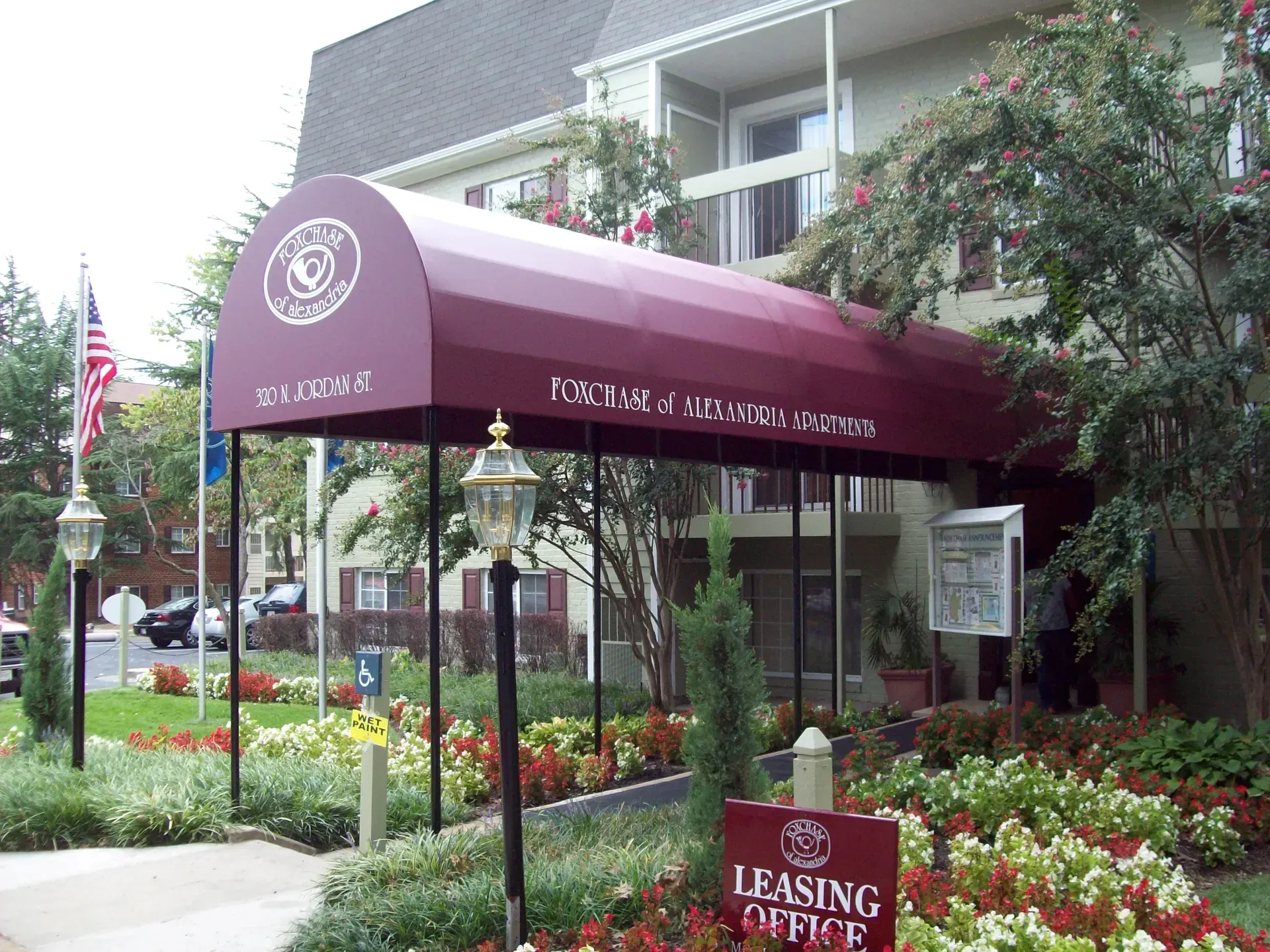 Maroon awning at an assisted living facility entrance surrounded by flower beds and greenery