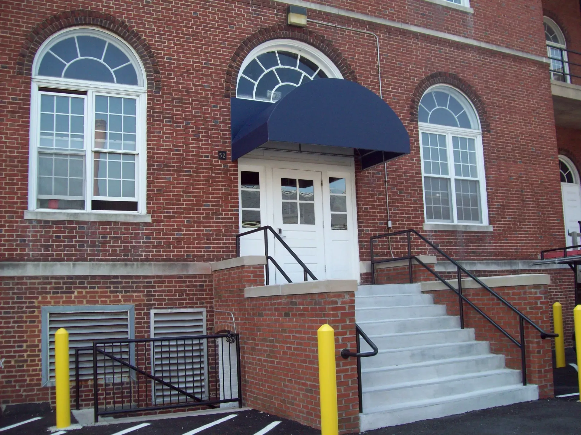Brick building entrance with blue awning, white steps, and black railings