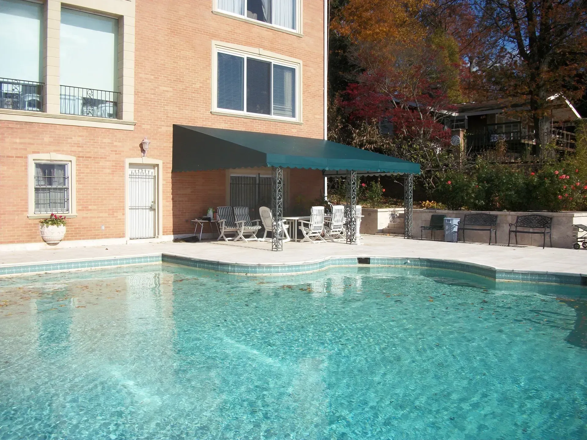 Outdoor swimming pool beside a brick building with lounge chairs and a shaded patio area
