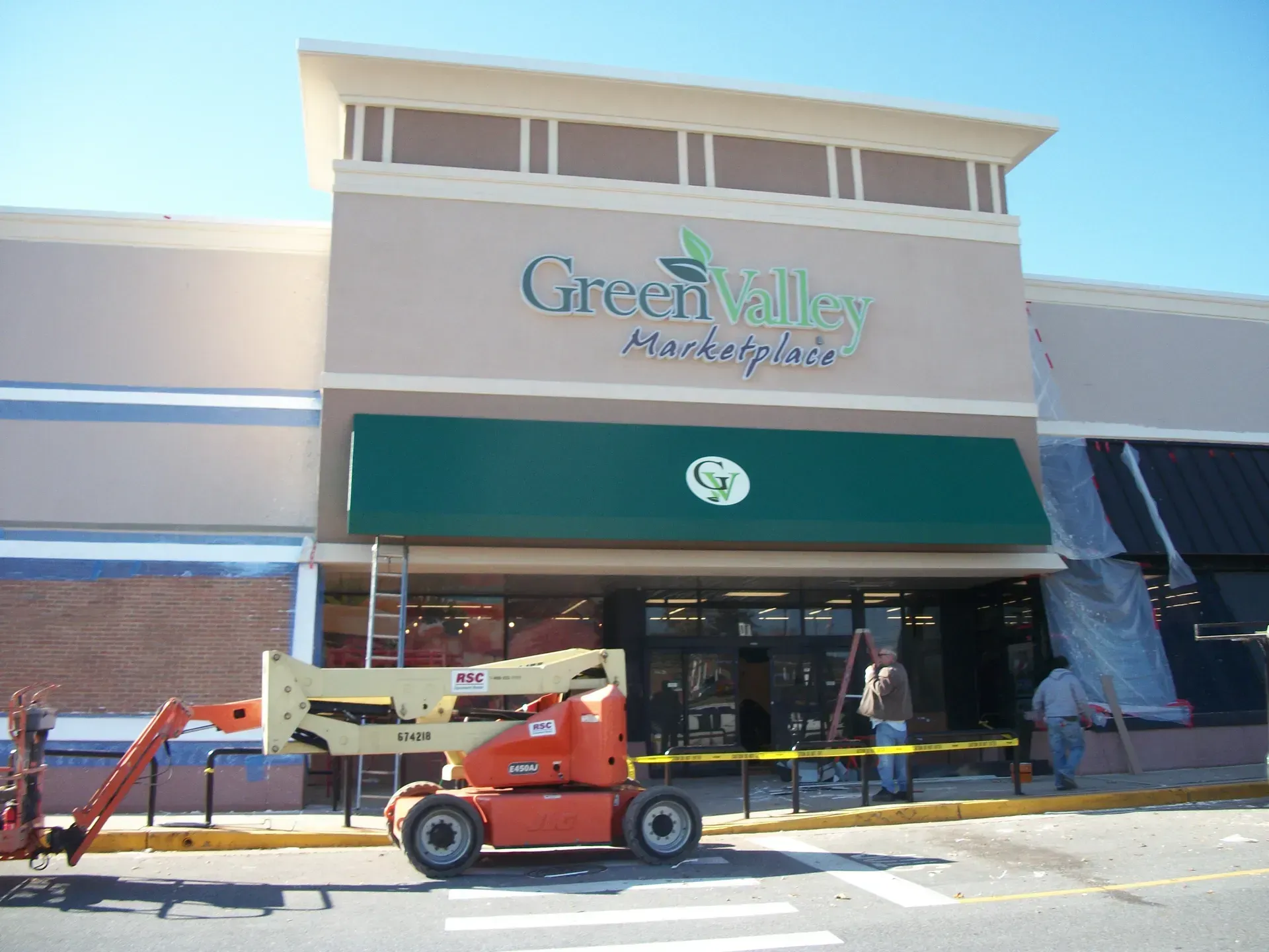 Storefront with a green awning and a lift parked outside, with construction work at the entrance.