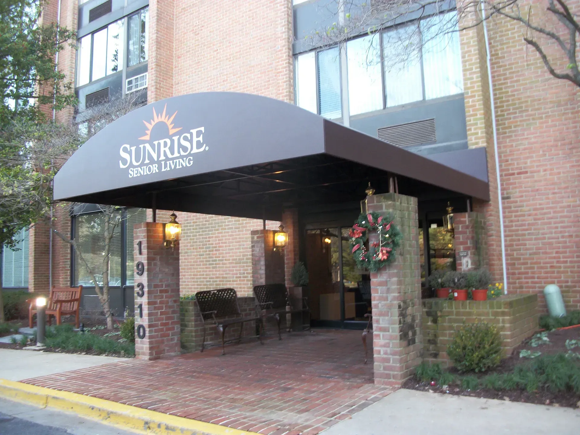 Sunrise Care Center entrance with black awning, brick walkway, and hanging plants