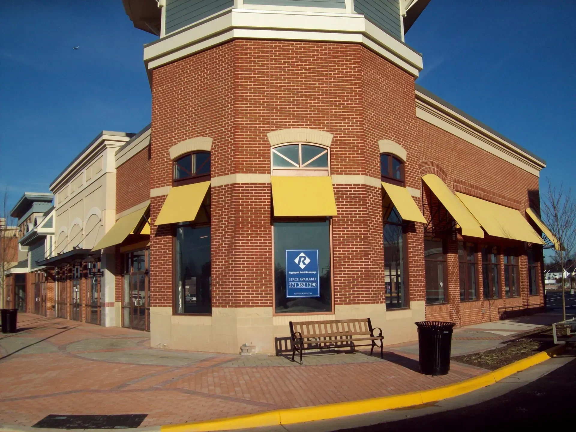 Brick corner storefront with yellow awnings and a blue sign on a sunny street corner