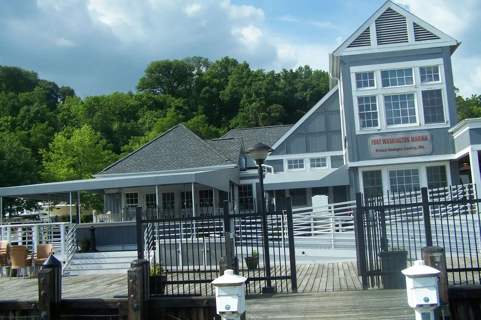 Blue-and-white waterfront building with a peaked roof, black fence, and outdoor seating near the water