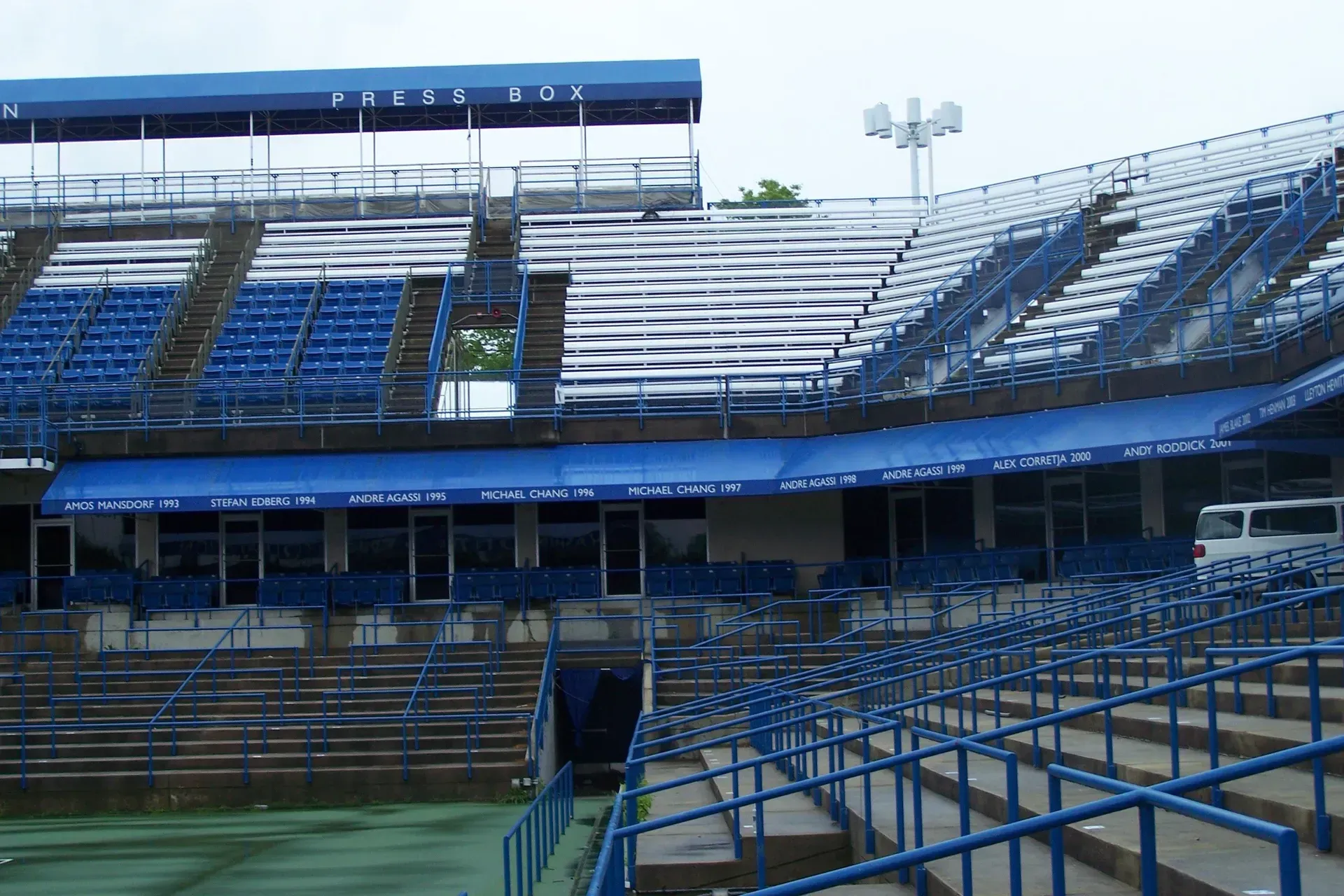 Empty blue stadium seating and bleachers under a roof, viewed from field level.