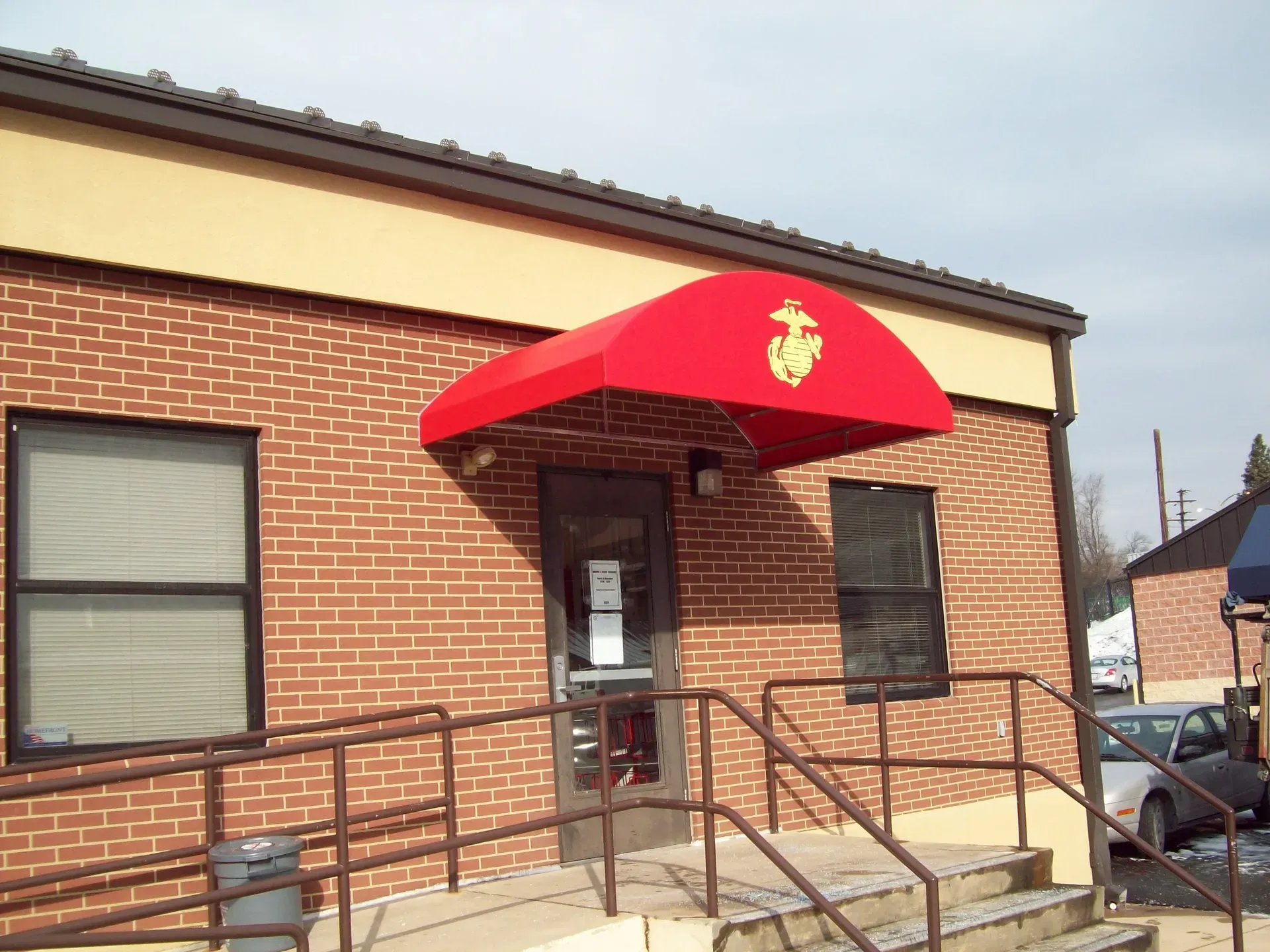 Brick building entrance with red awning and wheelchair ramp.