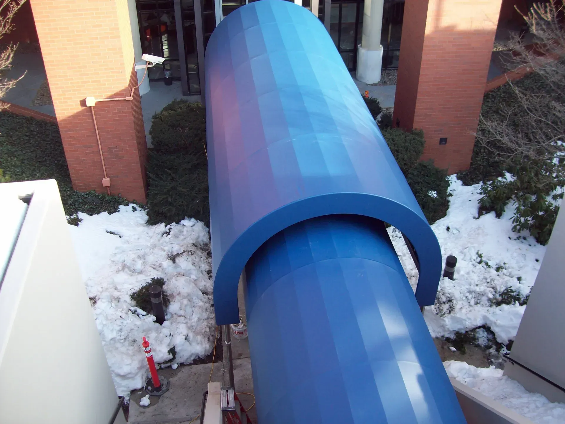 Blue pipe tunnel between brick buildings with snow on the ground