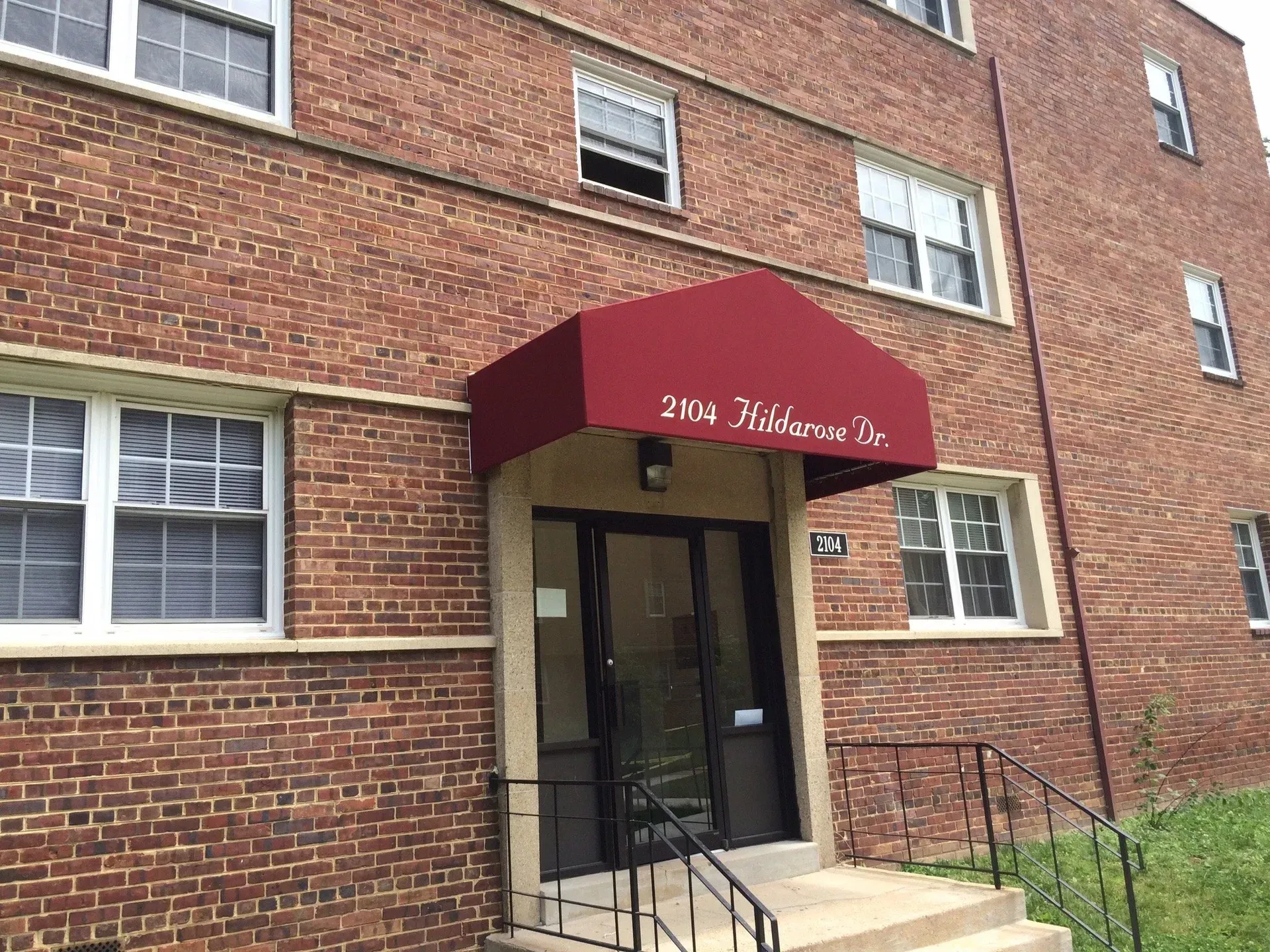 Brick apartment entrance with maroon awning and wheelchair-accessible ramp leading to glass doors