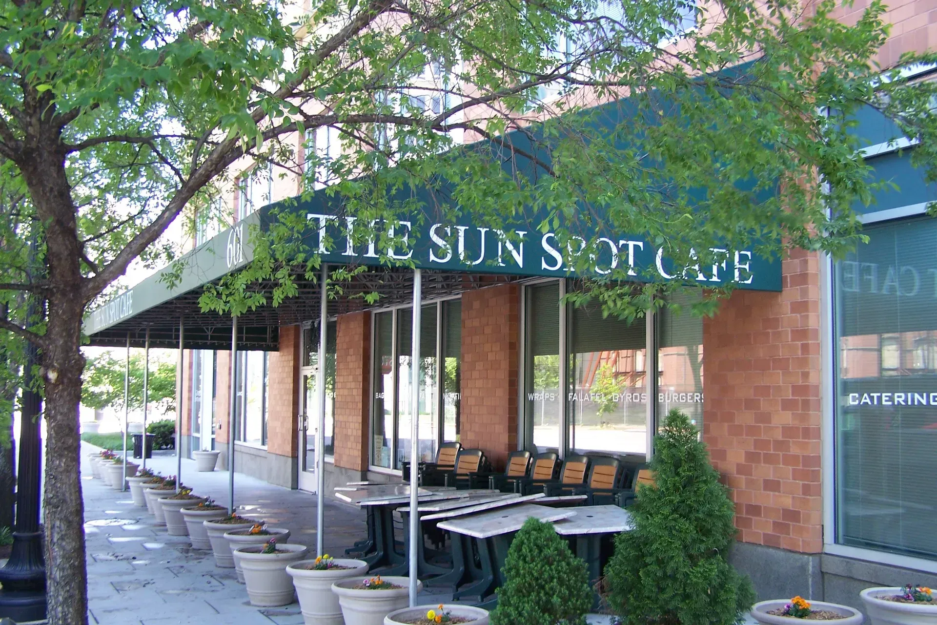 The Sun Spot Cafe storefront with outdoor seating and potted plants under a blue awning