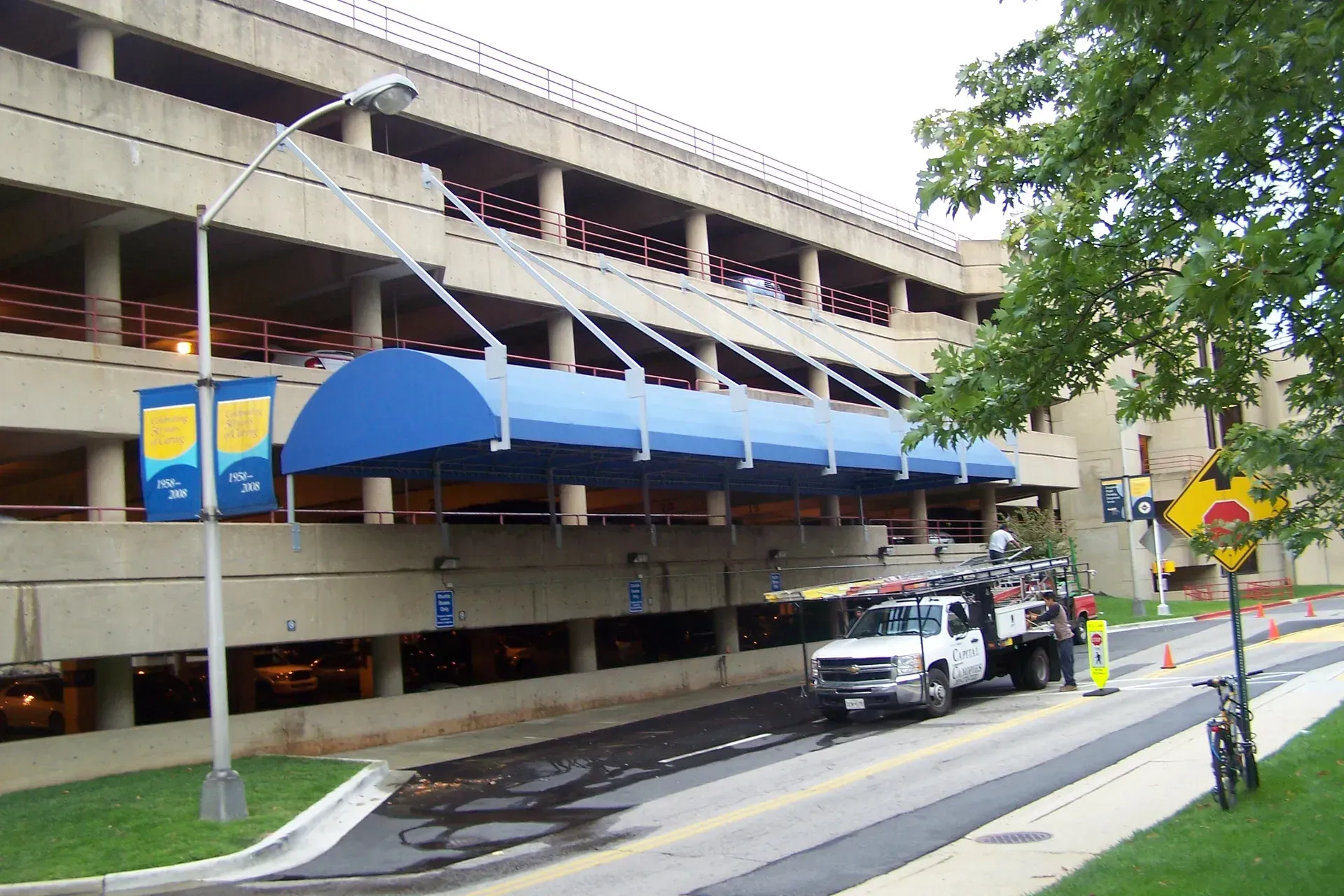 Covered street entrance with blue awning and parked vehicles beside a multi-level building