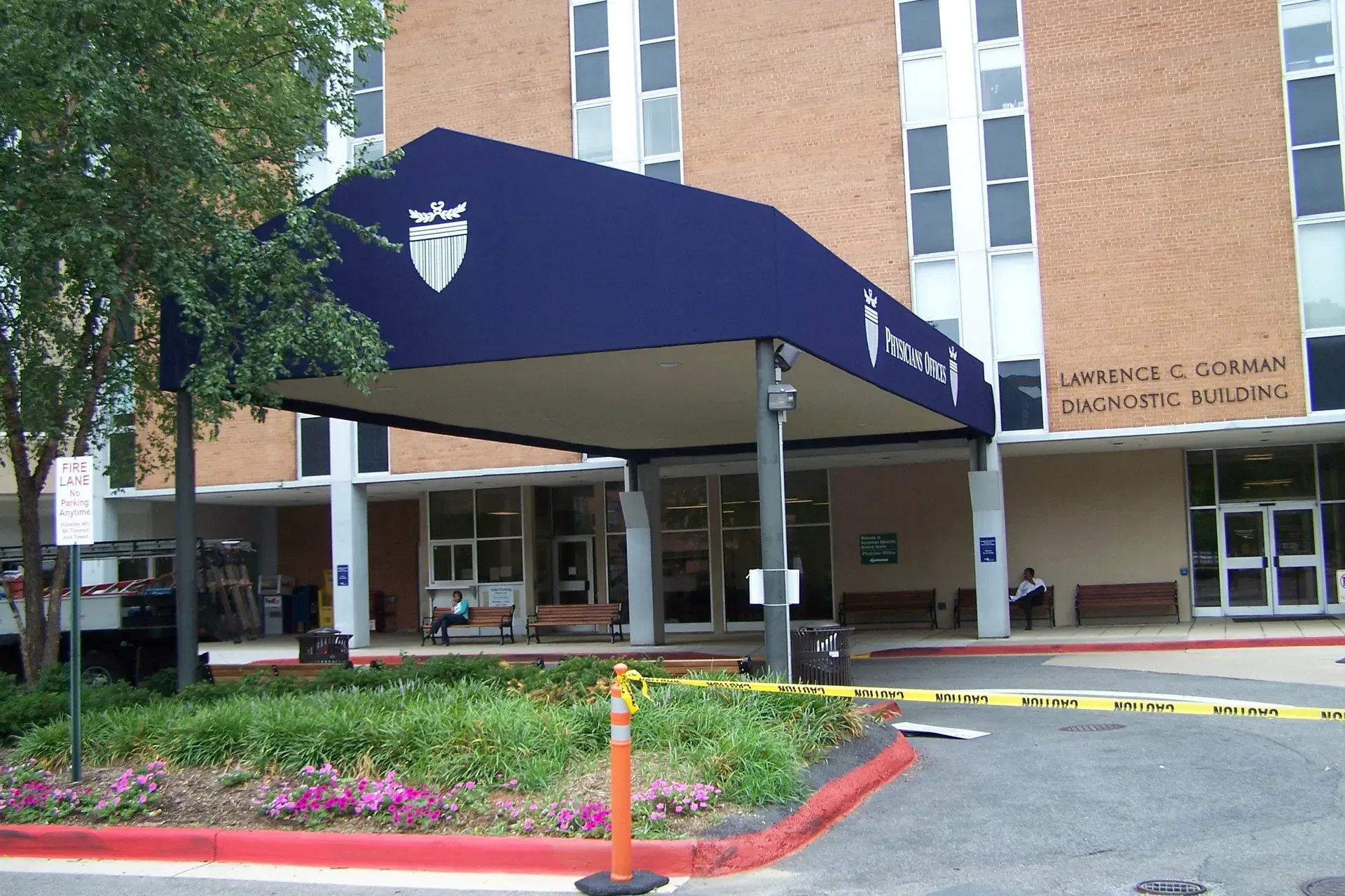 Hospital entrance with blue awning, brick building, and flower beds