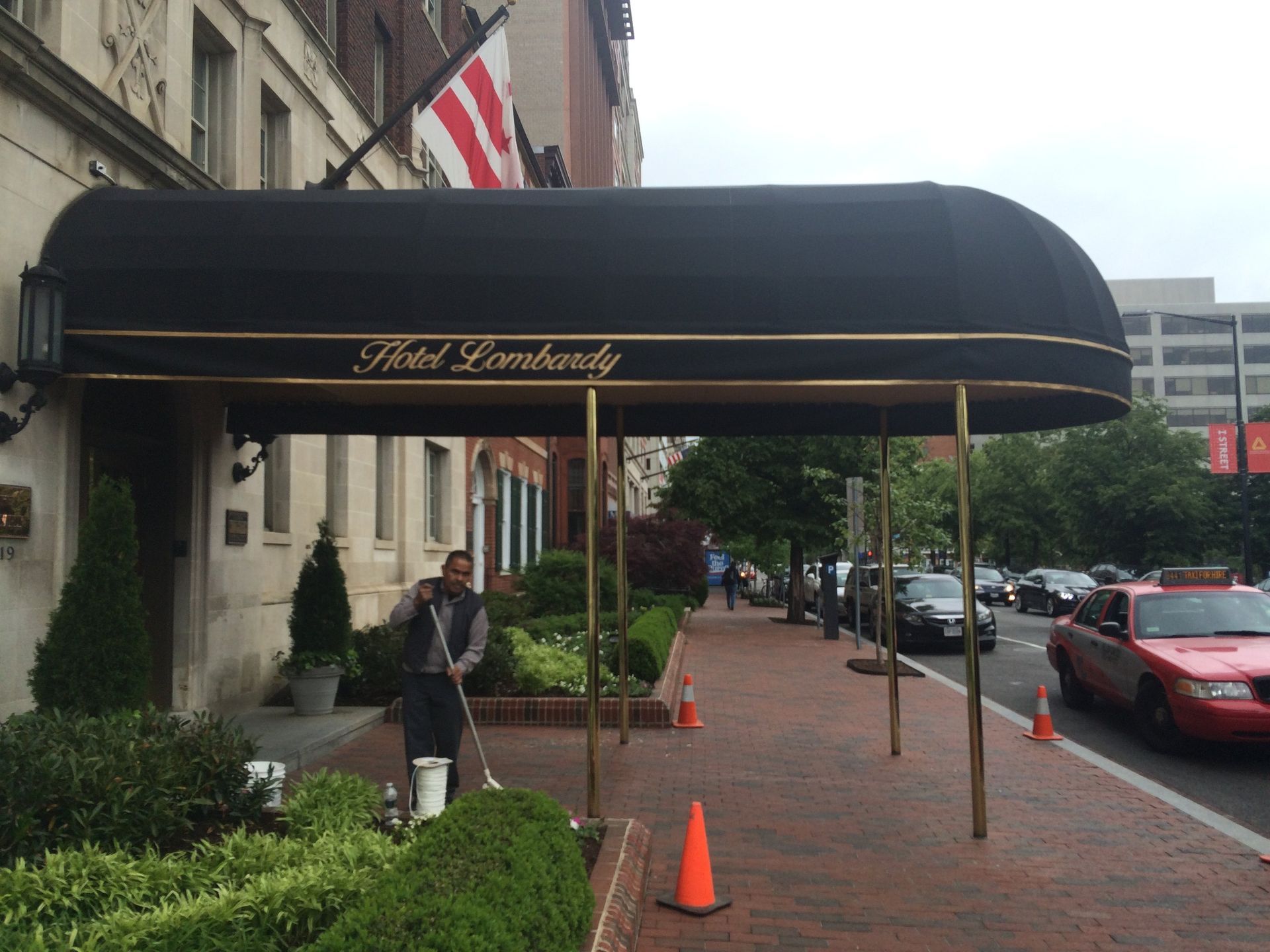 Hotel entrance with black awning, sidewalk cones, parked cars, and a person standing outside