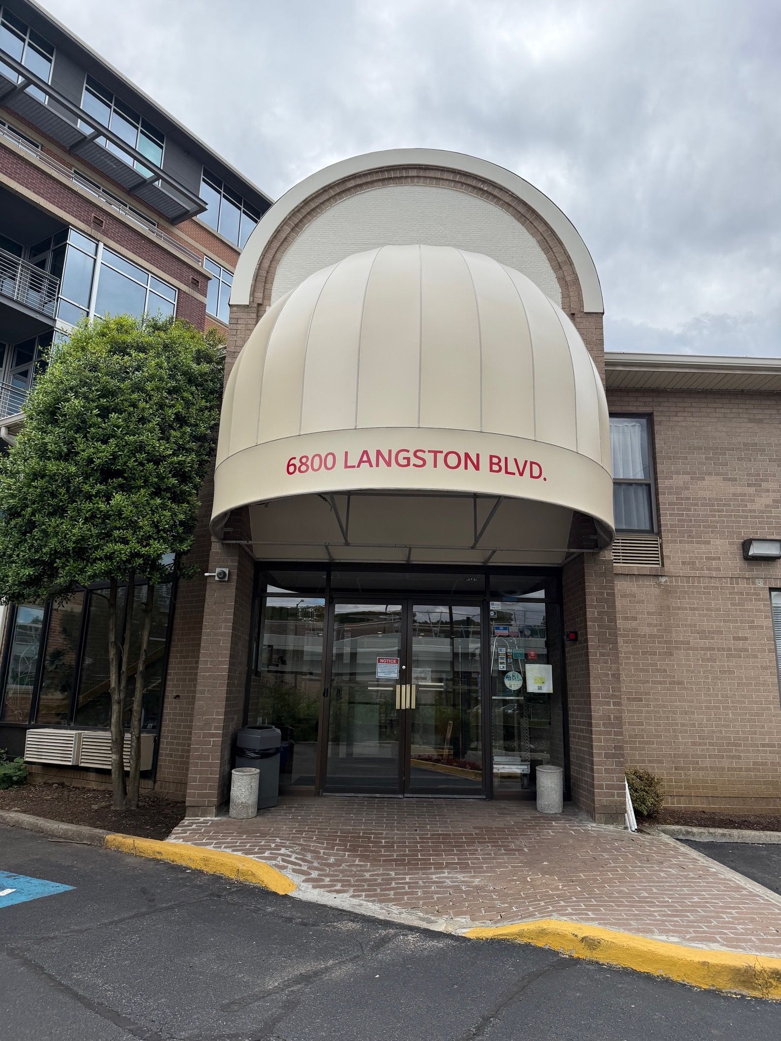Entrance to St. Luke's Chapel with glass doors and beige brick facade under cloudy skies.