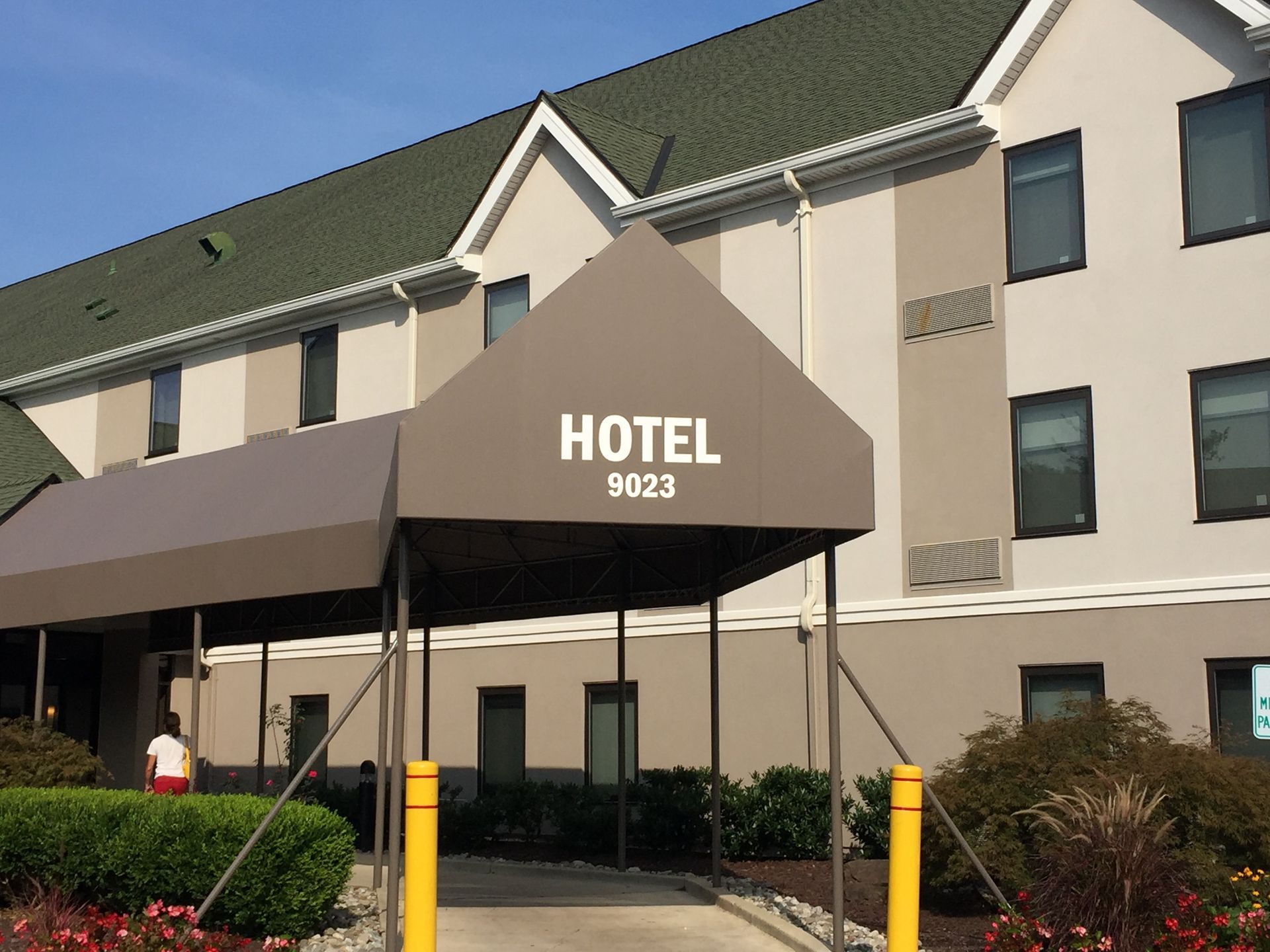 Hotel entrance with brown awning, white building, and landscaped shrubs.